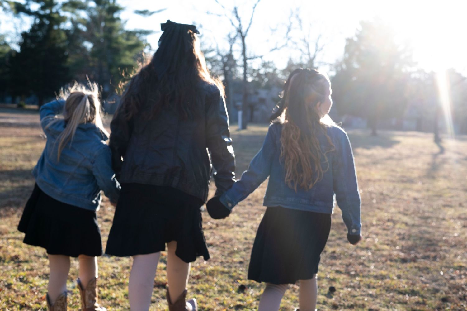 Family portrait of three girls holding hands in sunshine.