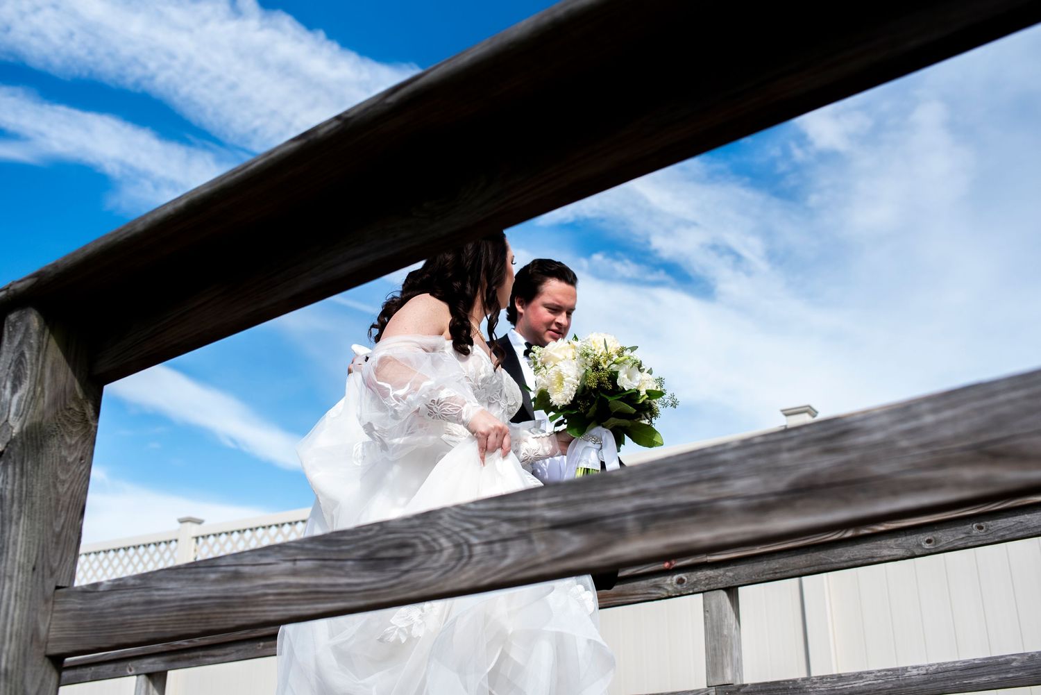 Wedding couple walks on Stone Harbor boardwalk, photographed from below through railing.