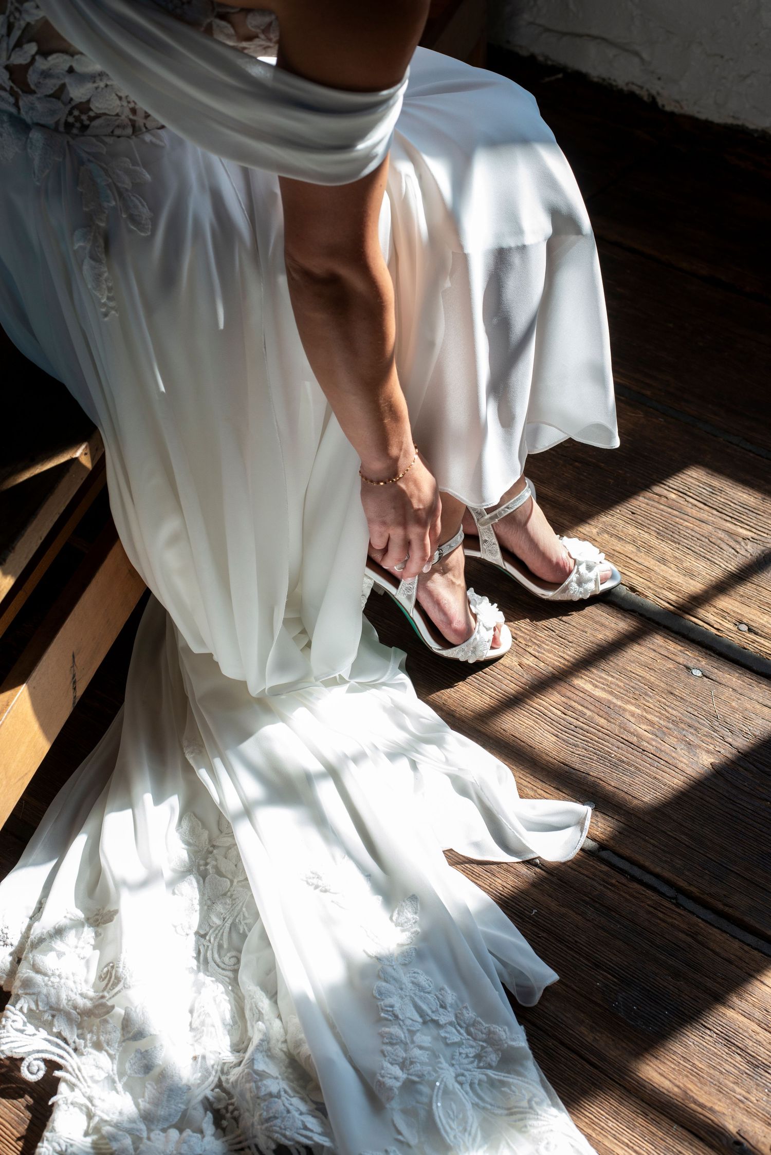Portrait of bride from knee down as she pulls on her shoes in the window light, getting ready at Bartram's Garden in Philadelphia, PA.