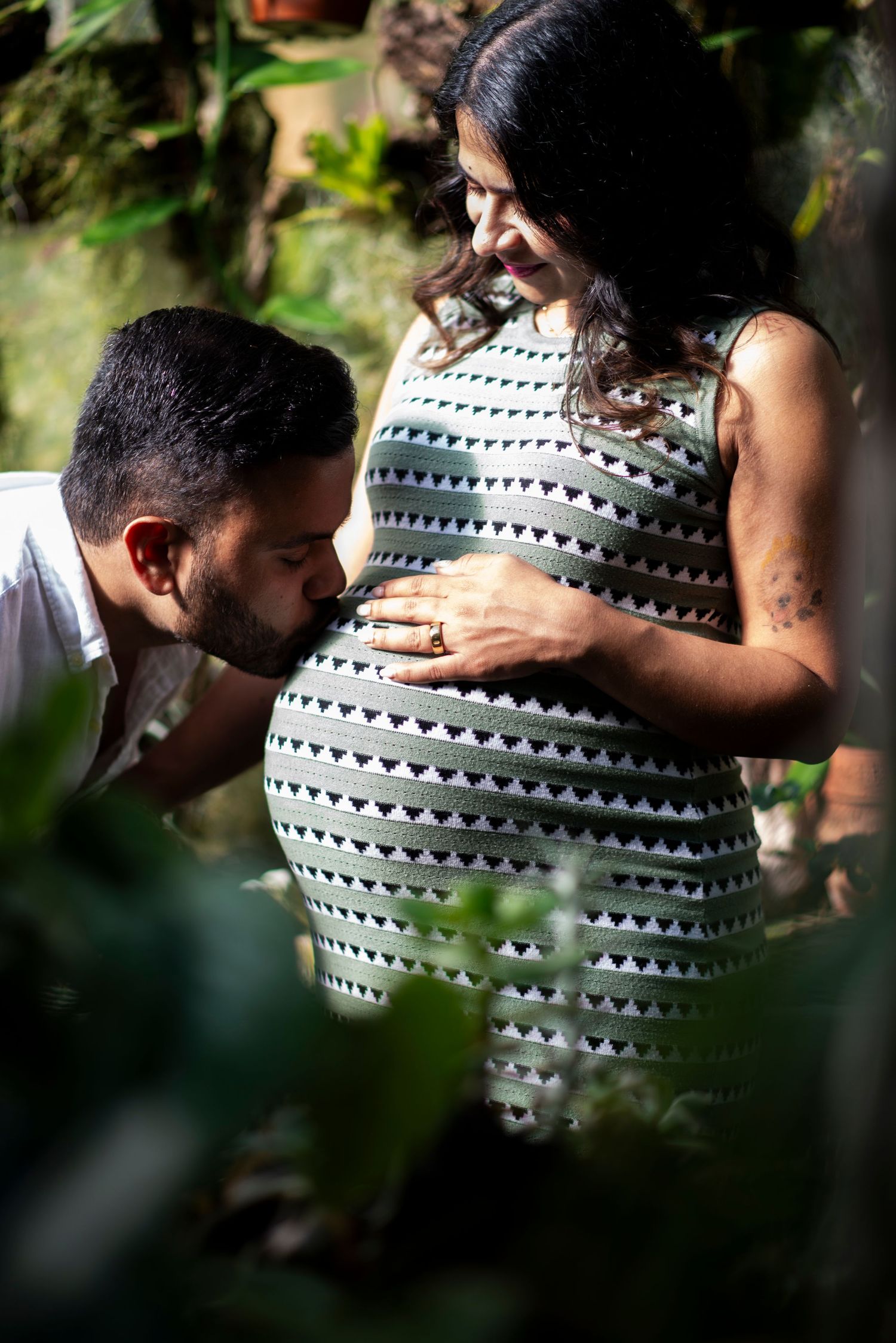 Man kisses pregnant wife's belly in the greenhouse at Deep Cut Gardens in New Jersey.