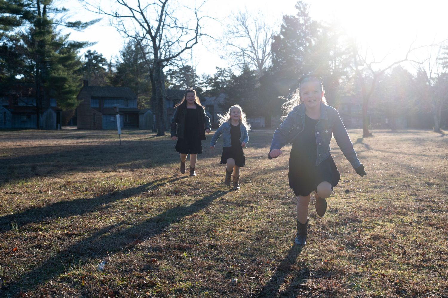 Three young girls run toward camera in bright sunshine at Batsto Historic Village in New Jersey.
