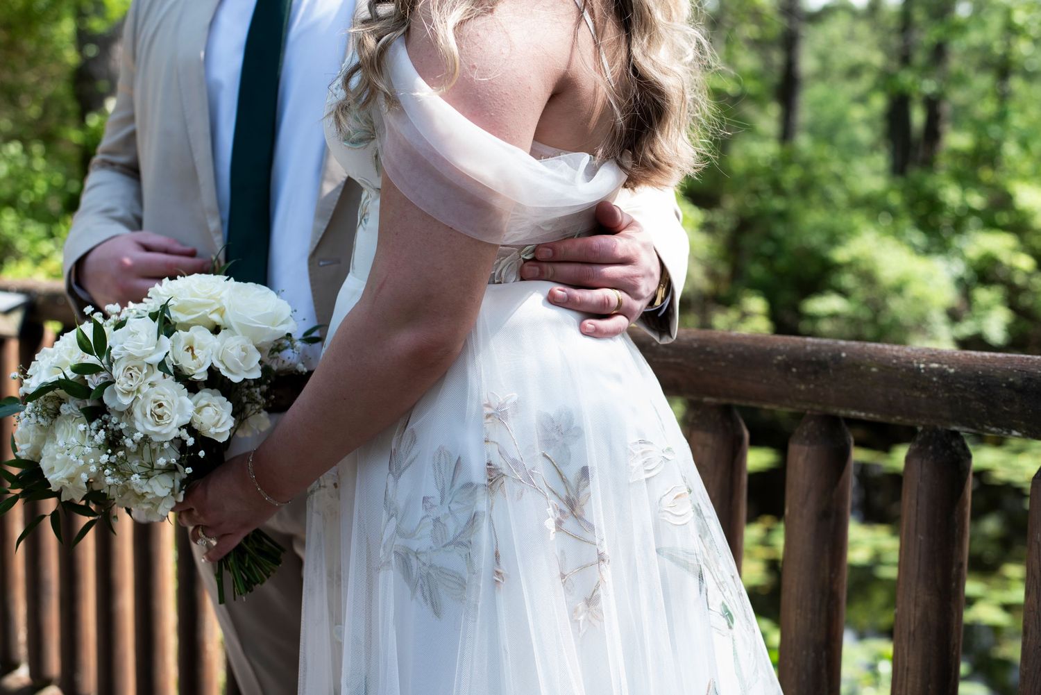 Close up of groom's hand on bride's back as they stand on the bridge during wedding portraits at Camp Matollionequay in Medford, New Jersey.