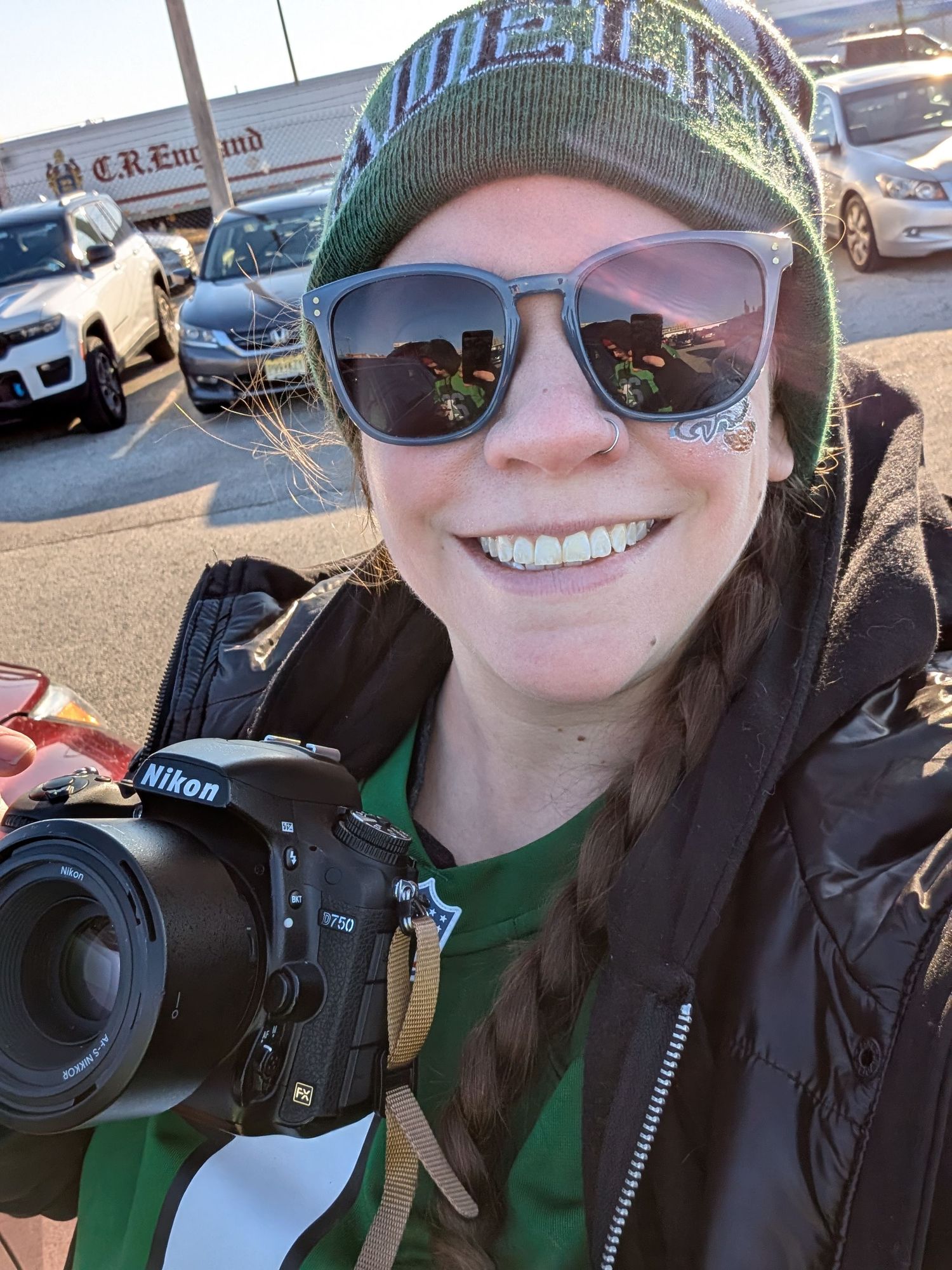 Selfie of woman in Philadelphia Eagles winter gear holding Nikon camera.