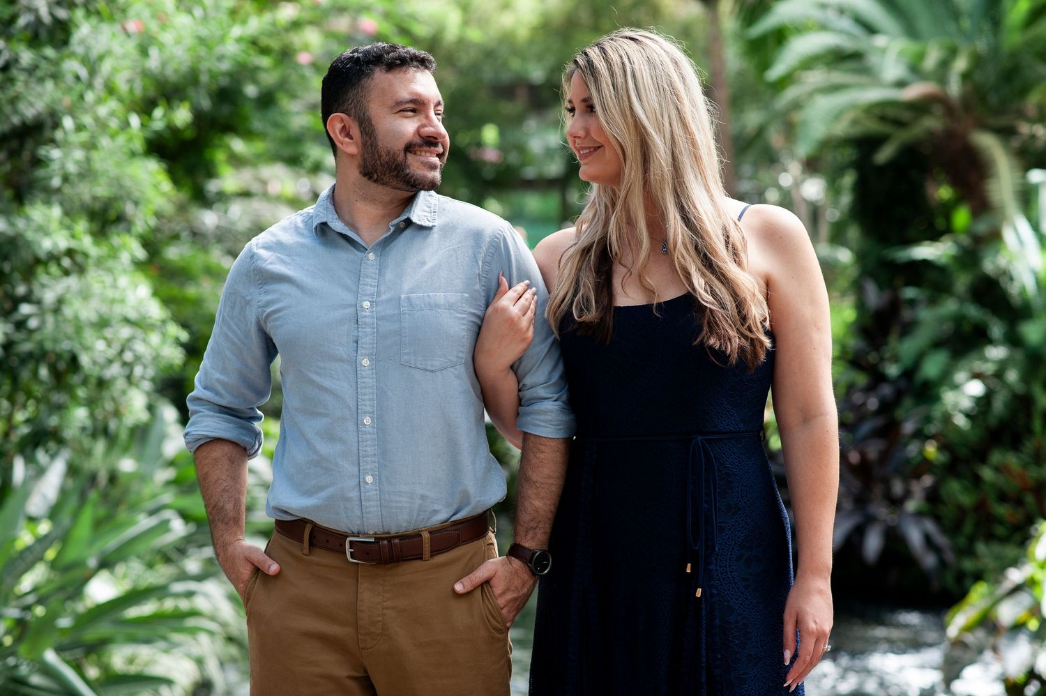 Engaged couple smile at each other, arm in arm in the conservatory at Longwood Gardens in Pennsylvania.