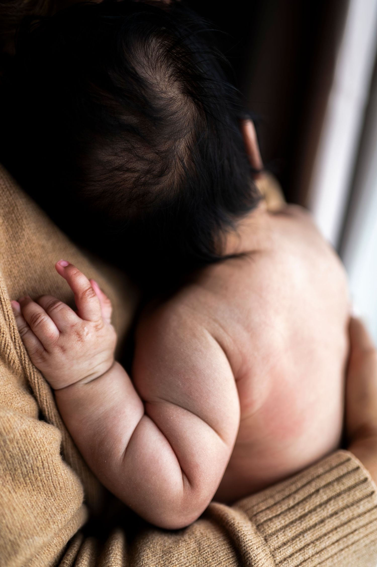 Closeup of newborn baby's arm and rolls in her skin as she's held by her mother.
