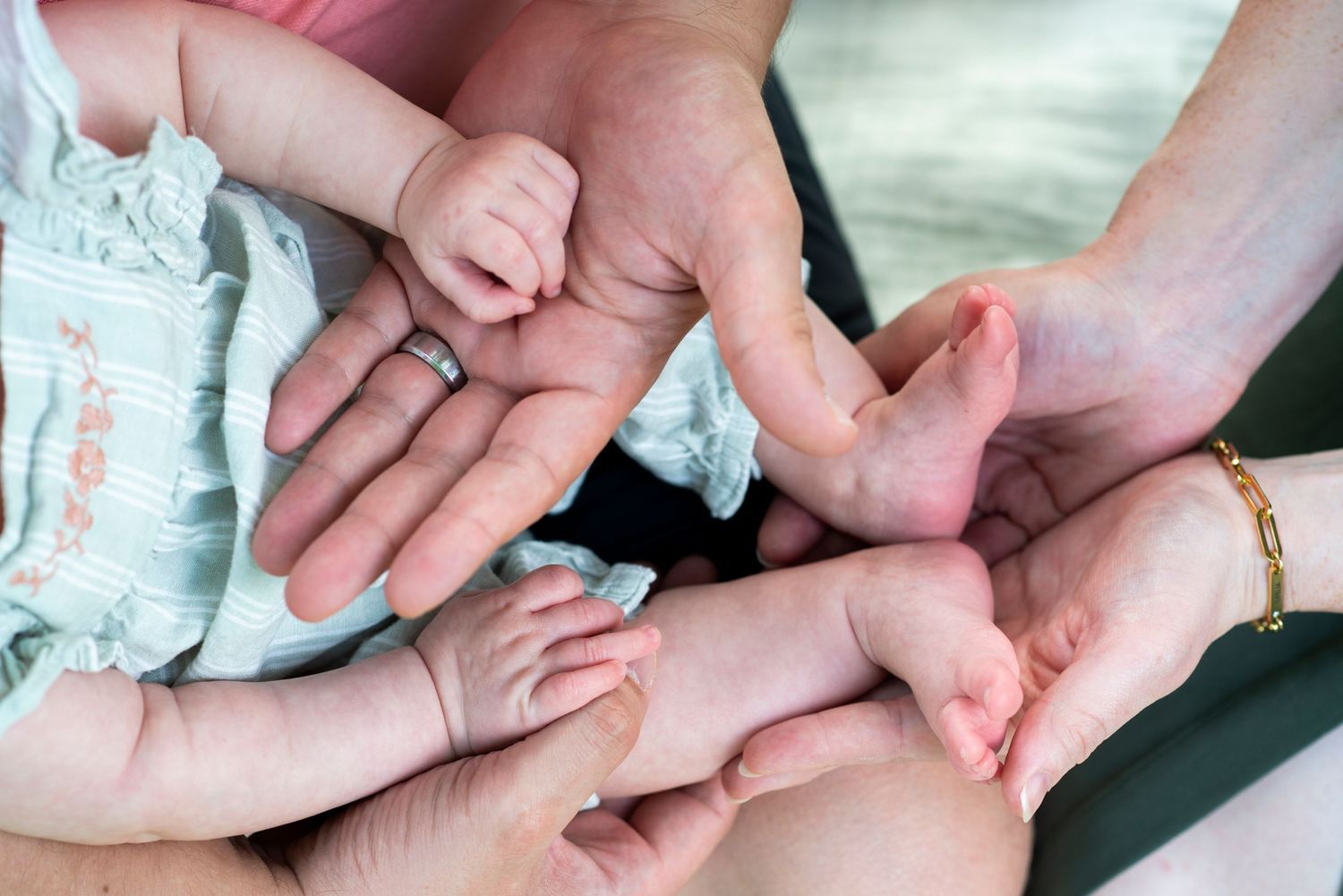 Close up of parents hands holding infant's hands and feet on their laps.
