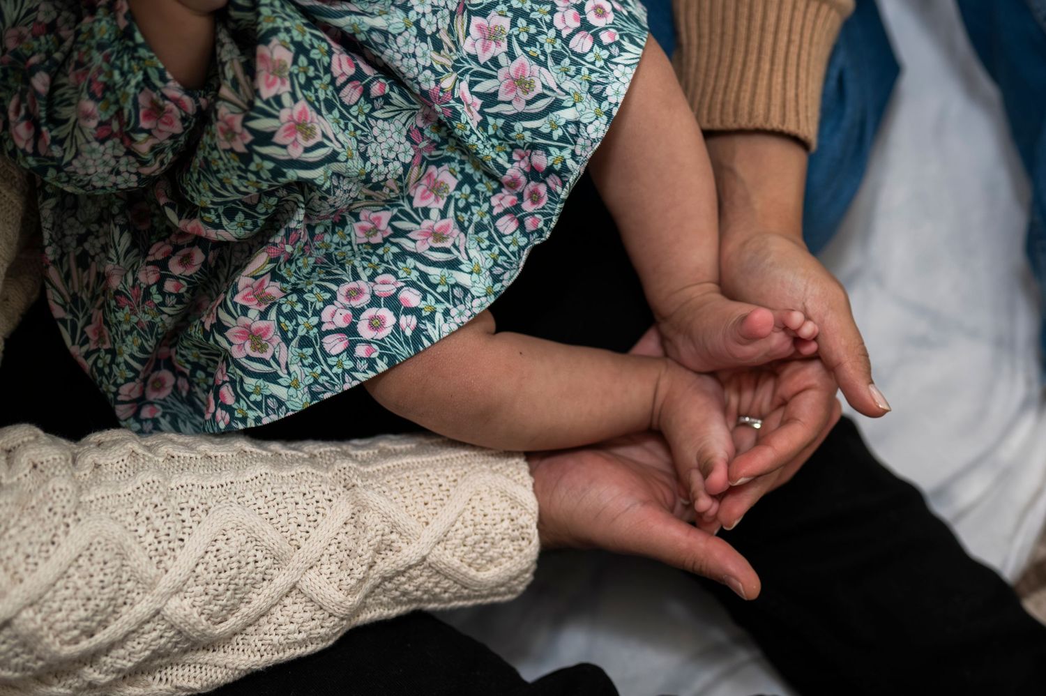 New parents hold their daughter's feet on their lap from above.