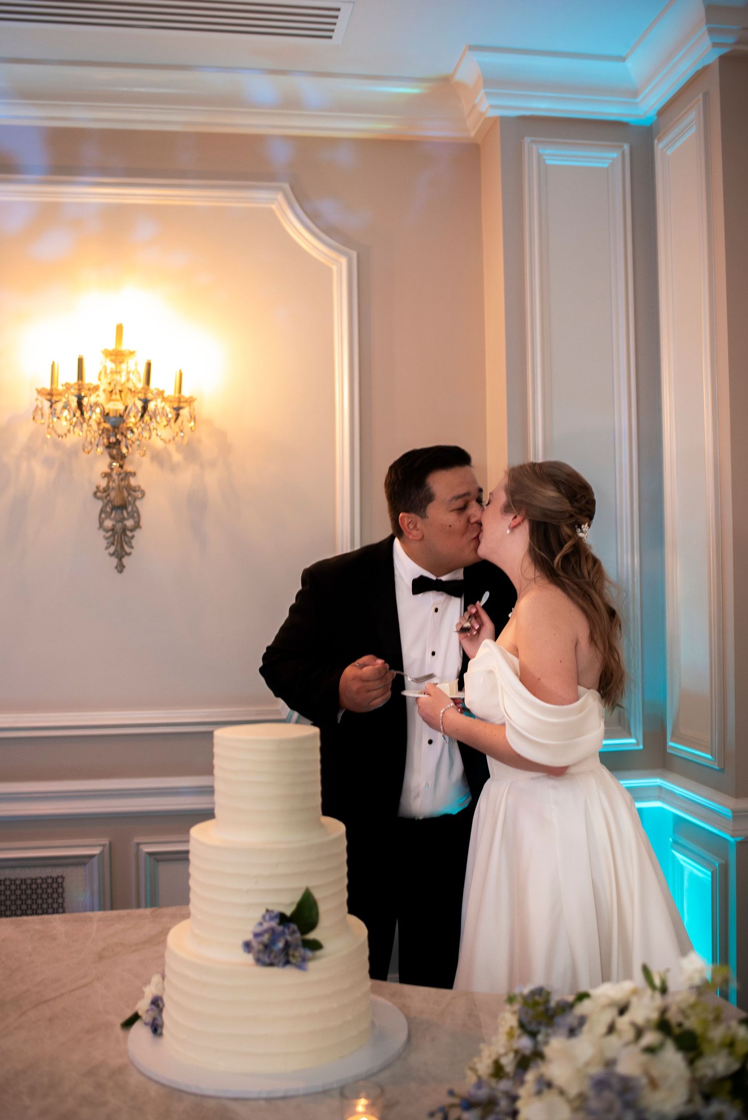 Bride and groom kiss behind their cake during wedding reception at The Mansion in Voorhees, New Jersey.