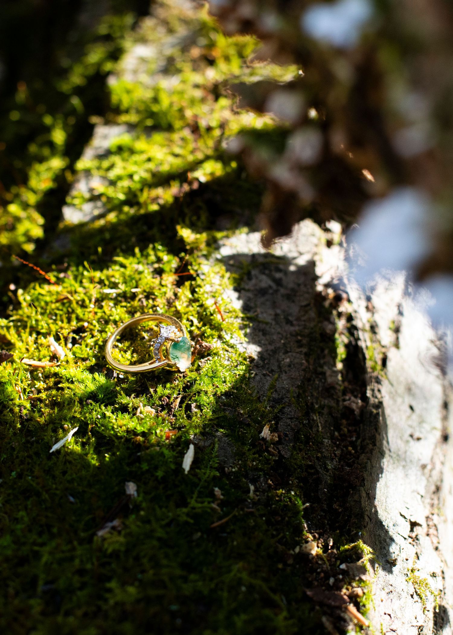 Emerald engagement ring shines in the sun on a mossy rock in Hawk Falls, PA.