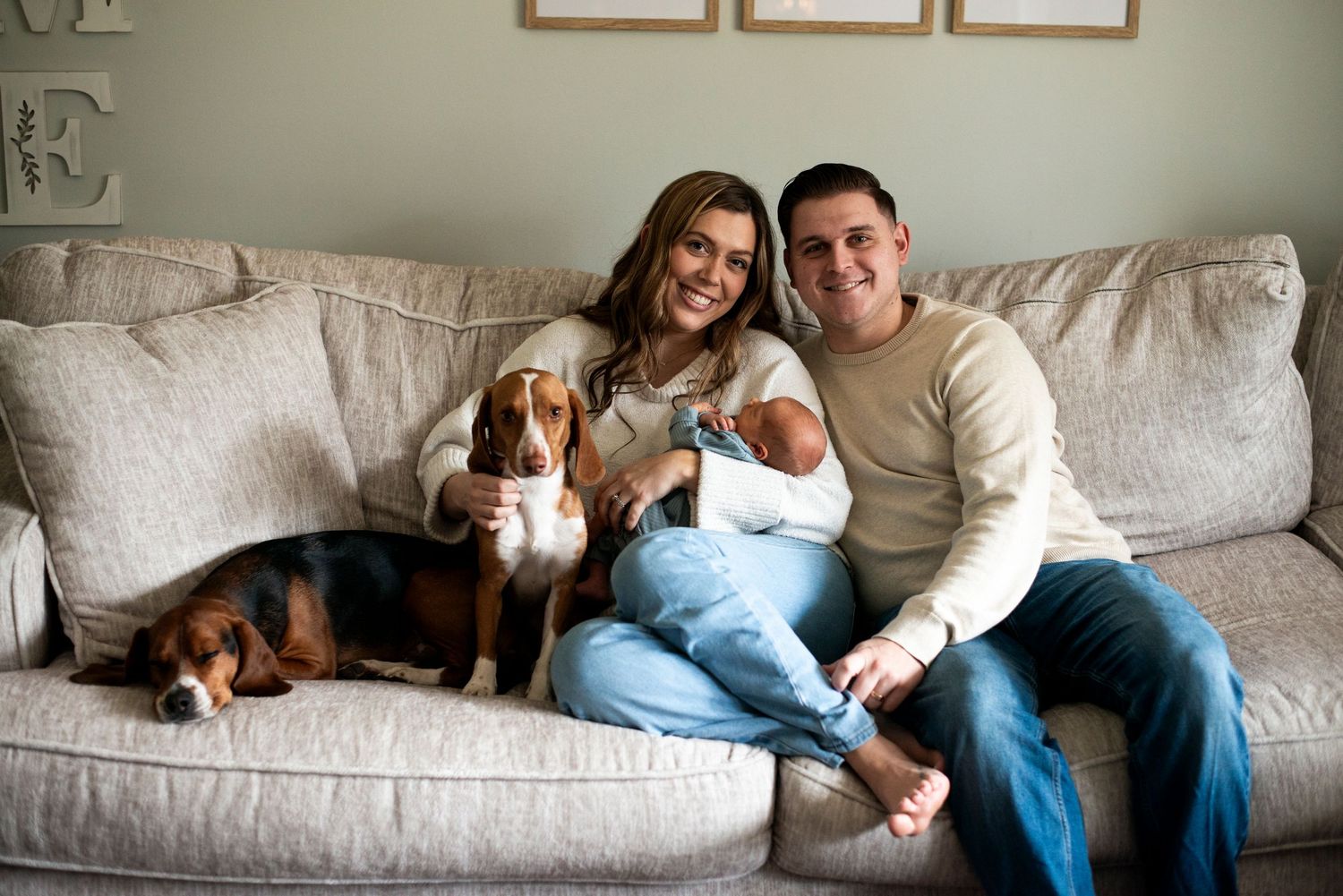 New parents hold their newborn son and sit with their two beagles on the couch in their Medford, New Jersey home.