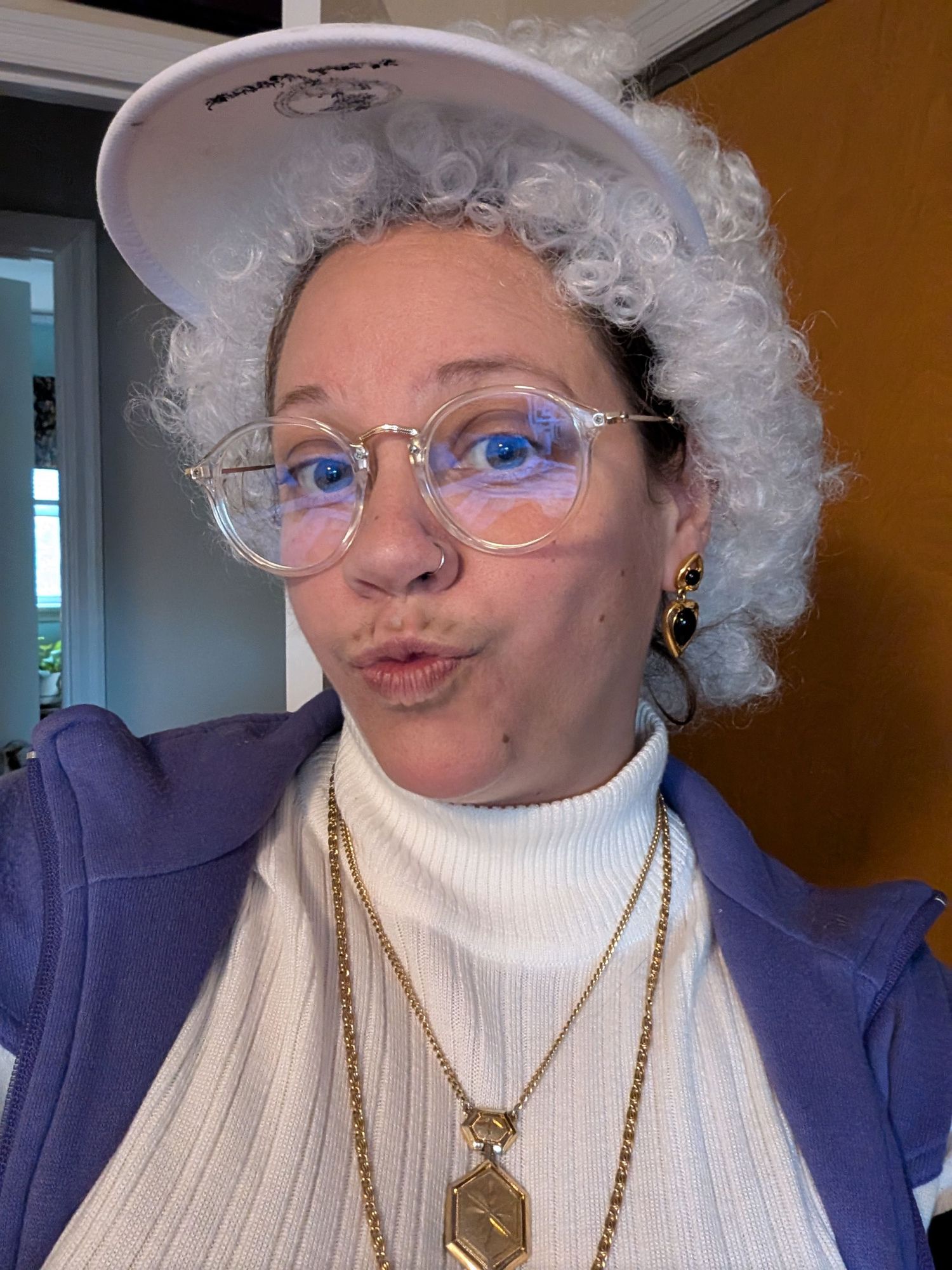 Selfie of woman in a white wig with big glasses, a visor and a turtleneck.