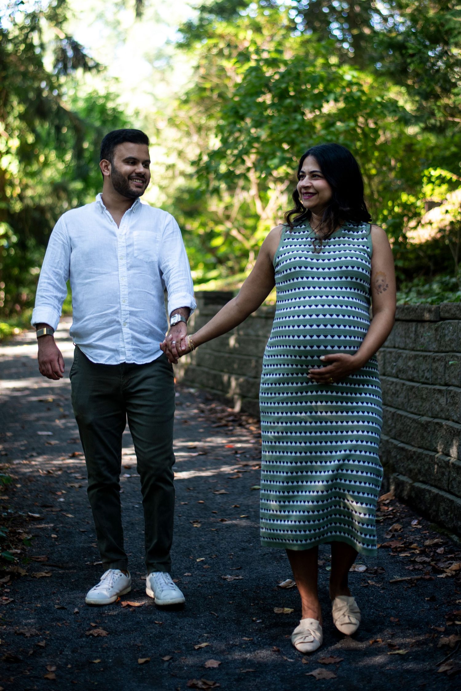 Couple holds hands while walking on path at Deep Cut Gardens in New Jersey during maternity shoot.