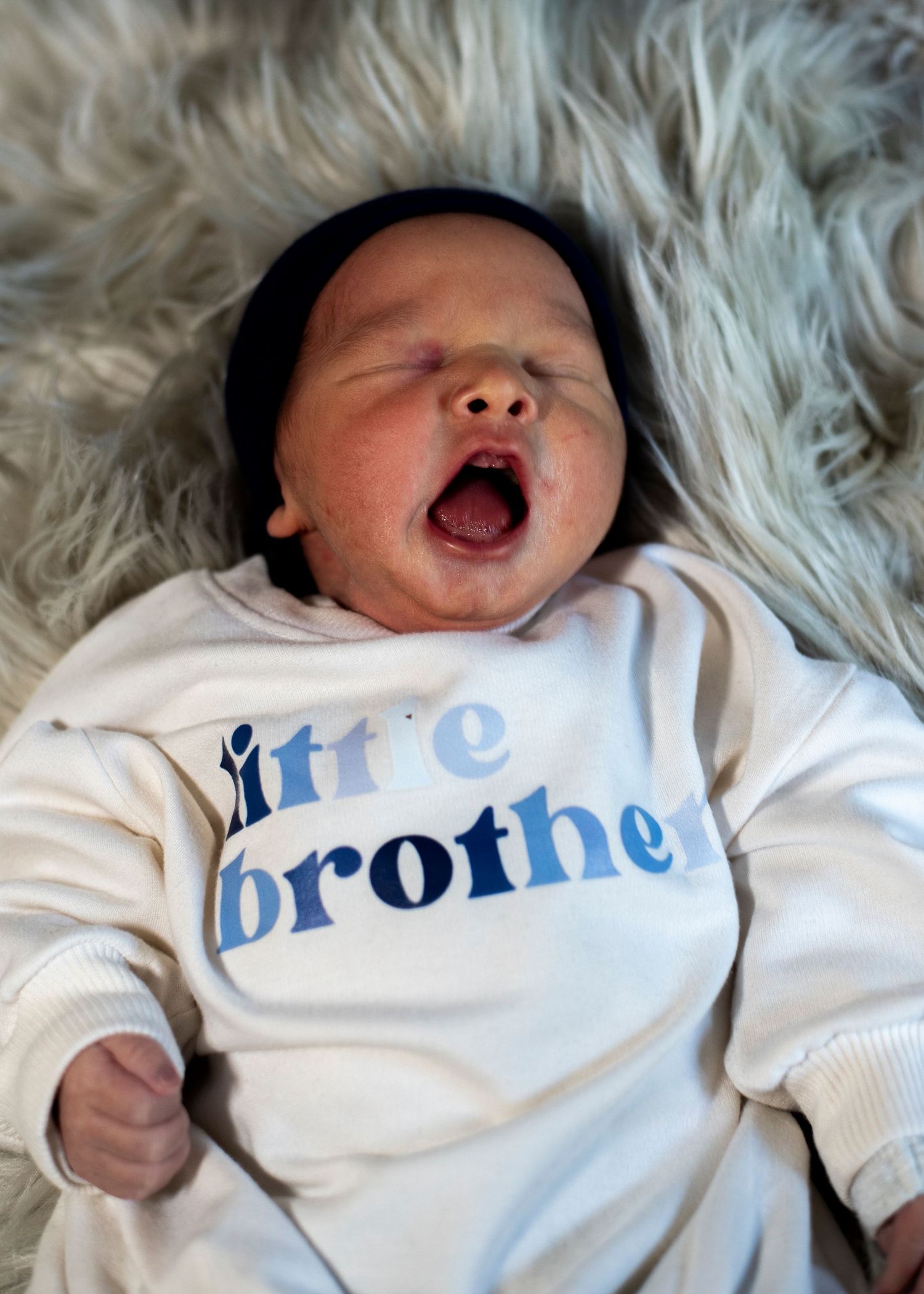 Portrait of newborn baby boy yawning in his Little Brother onesie.