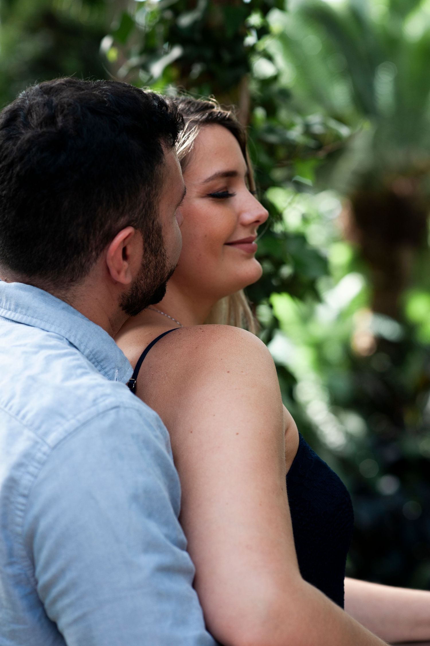 Engaged couple embraces with eyes closed among greenery at Longwood Gardens in Pennsylvania.