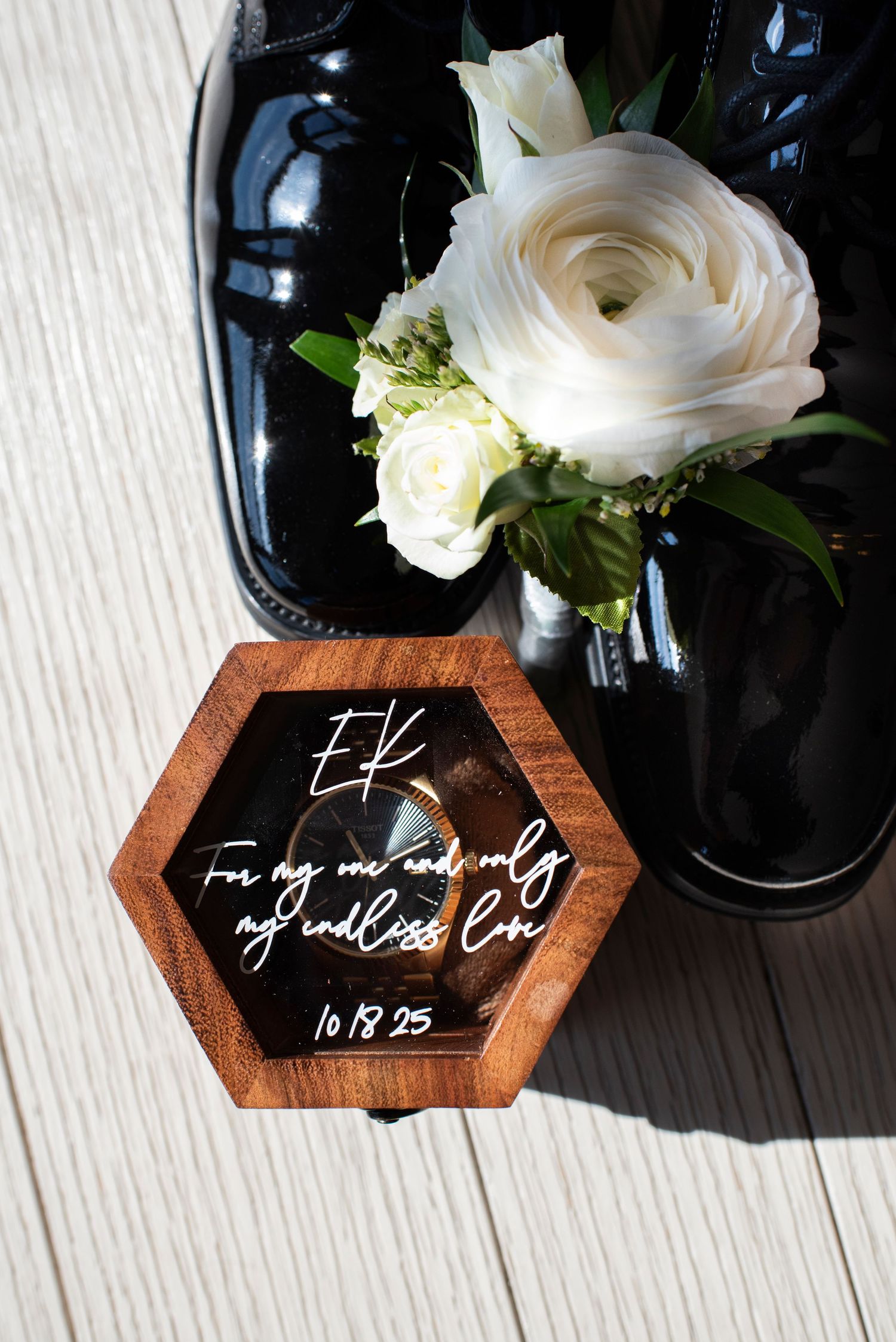 Detail closeup of groom's boutonniere sitting on his shoes next to new watch with engraving from his future wife.