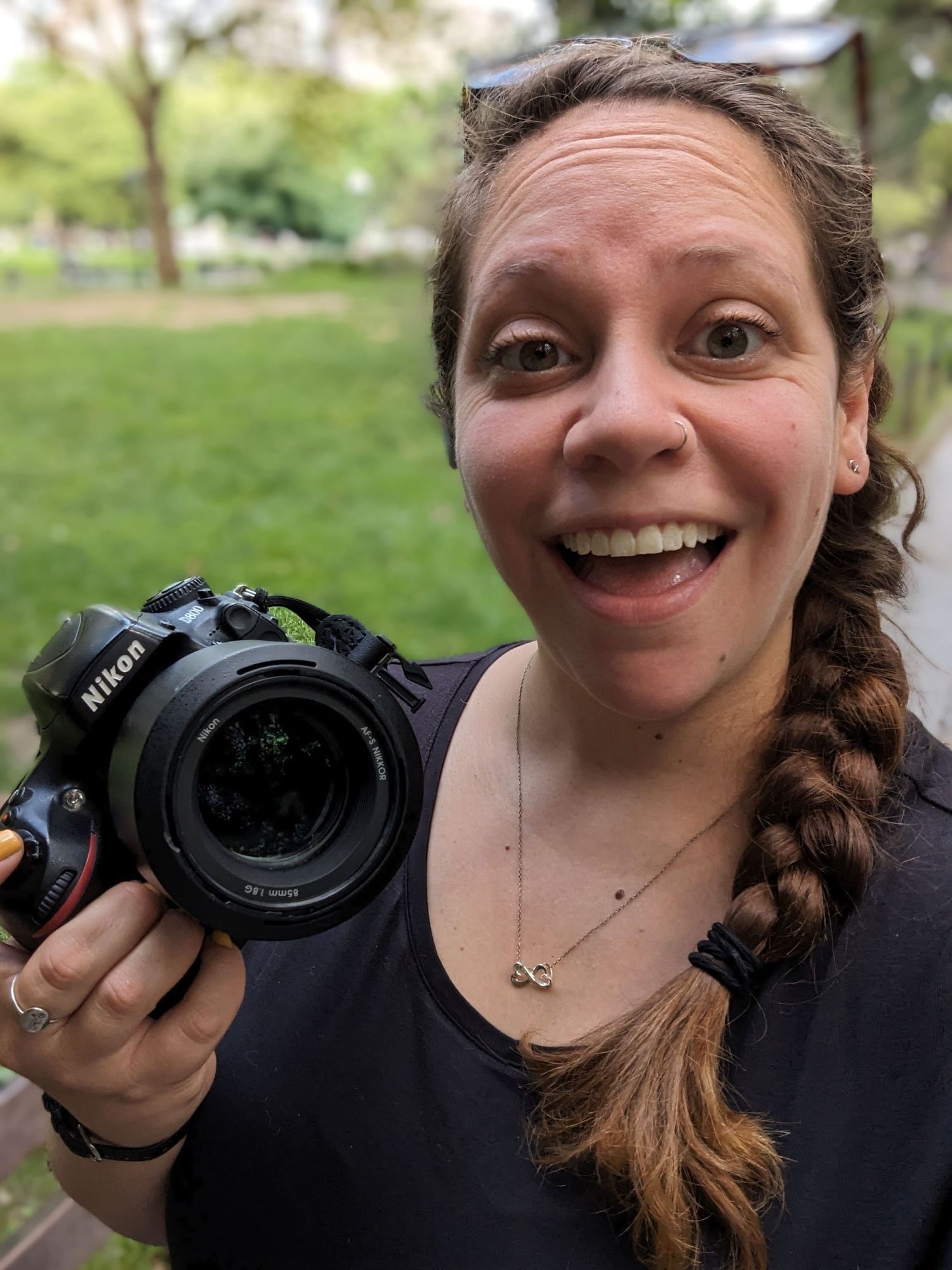 Selfie of photographer with side braid holding Nikon camera outside.
