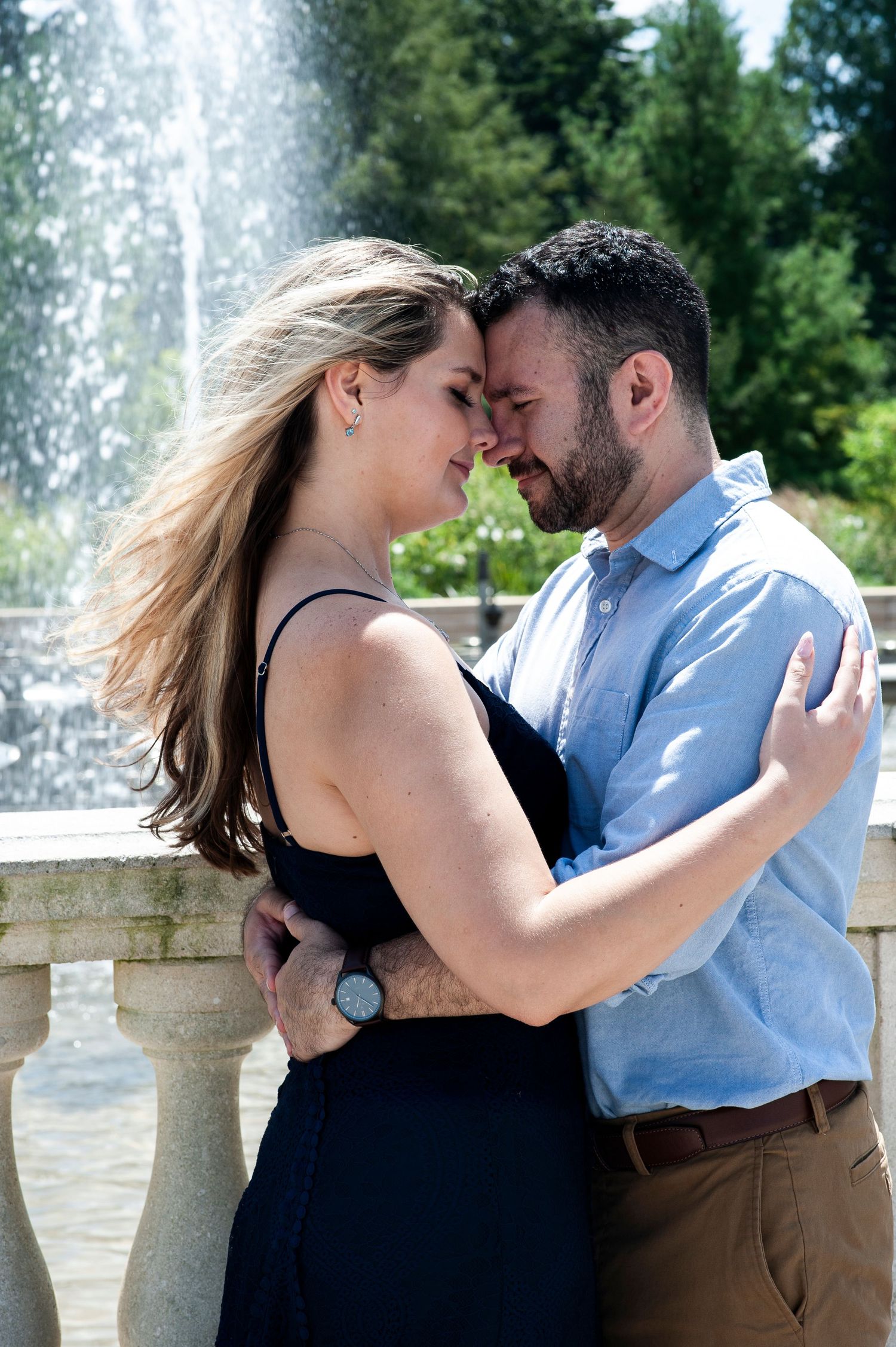Engaged couple touch foreheads with eyes closed in front of a fountain at Longwood Gardens in Pennsylvania.