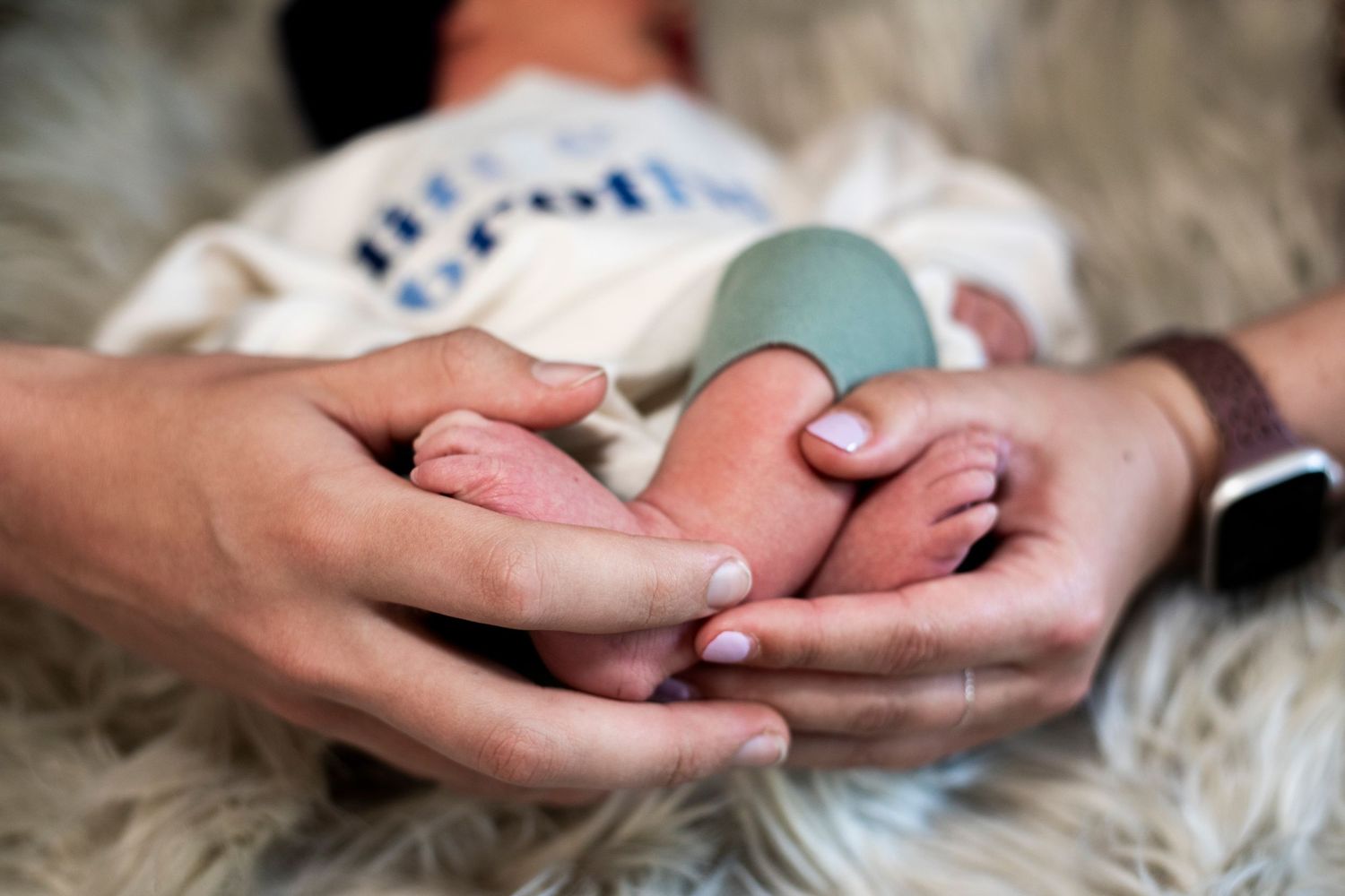 Close up of parents' hands holding newborn baby's feet.