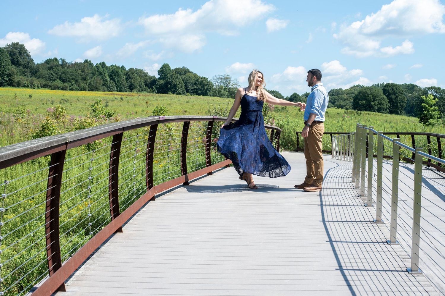 Engaged couple twirls on a bridge through a beautiful field at Longwood Gardens in Pennsylvania.