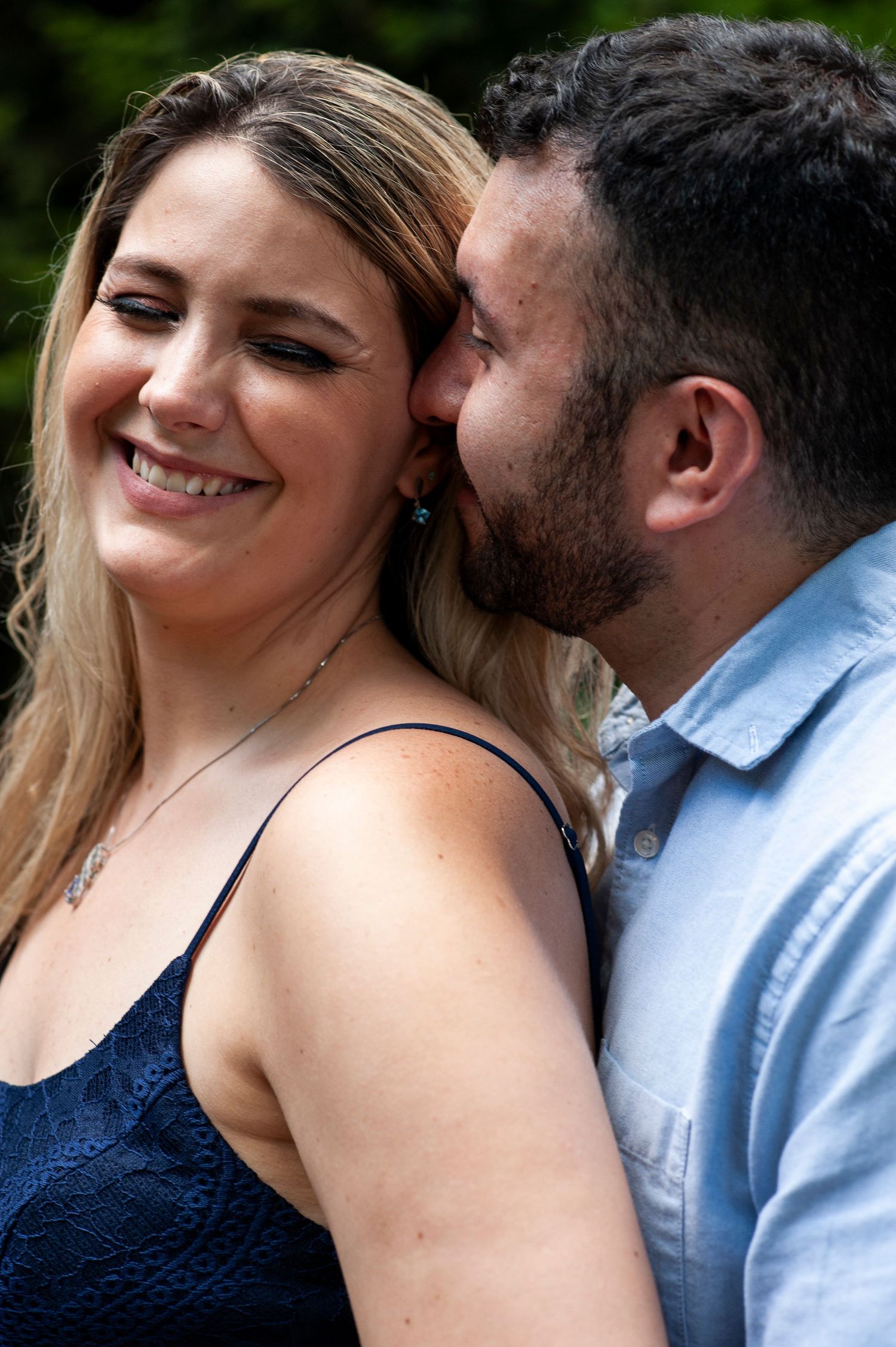 Woman smiles as her future husband whispers in her ear during their engagement shoot at Longwood Gardens in Pennsylvania.