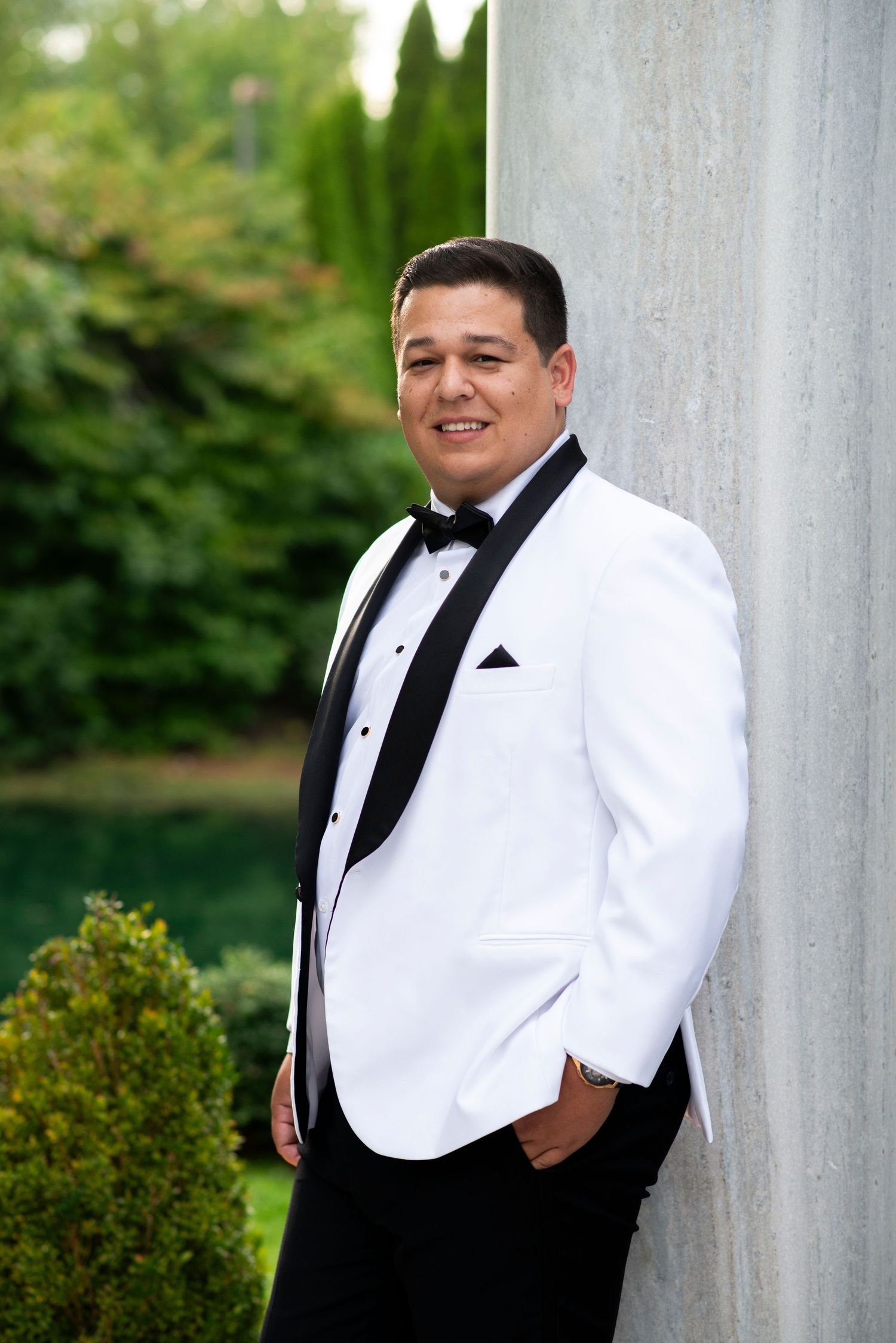 Groom leans against an outdoor column for a portrait in the garden at the Mansion in Voorhees, New Jersey.