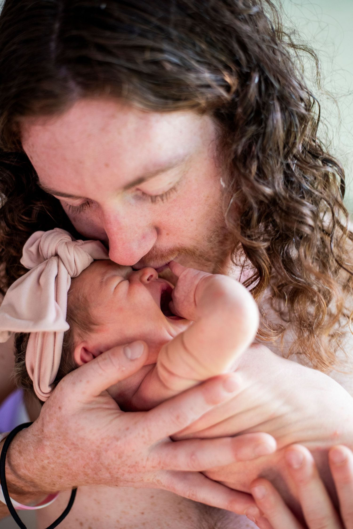 New father closes his eyes as he holds his newborn daughter for a kiss.