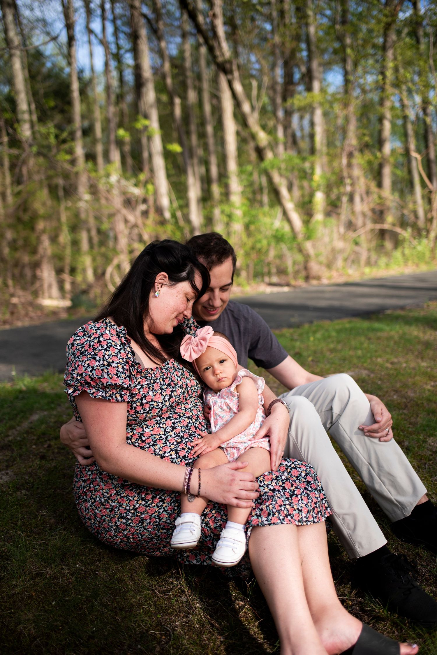 Family of three snuggles on the grass during maternity photoshoot in New Jersey.