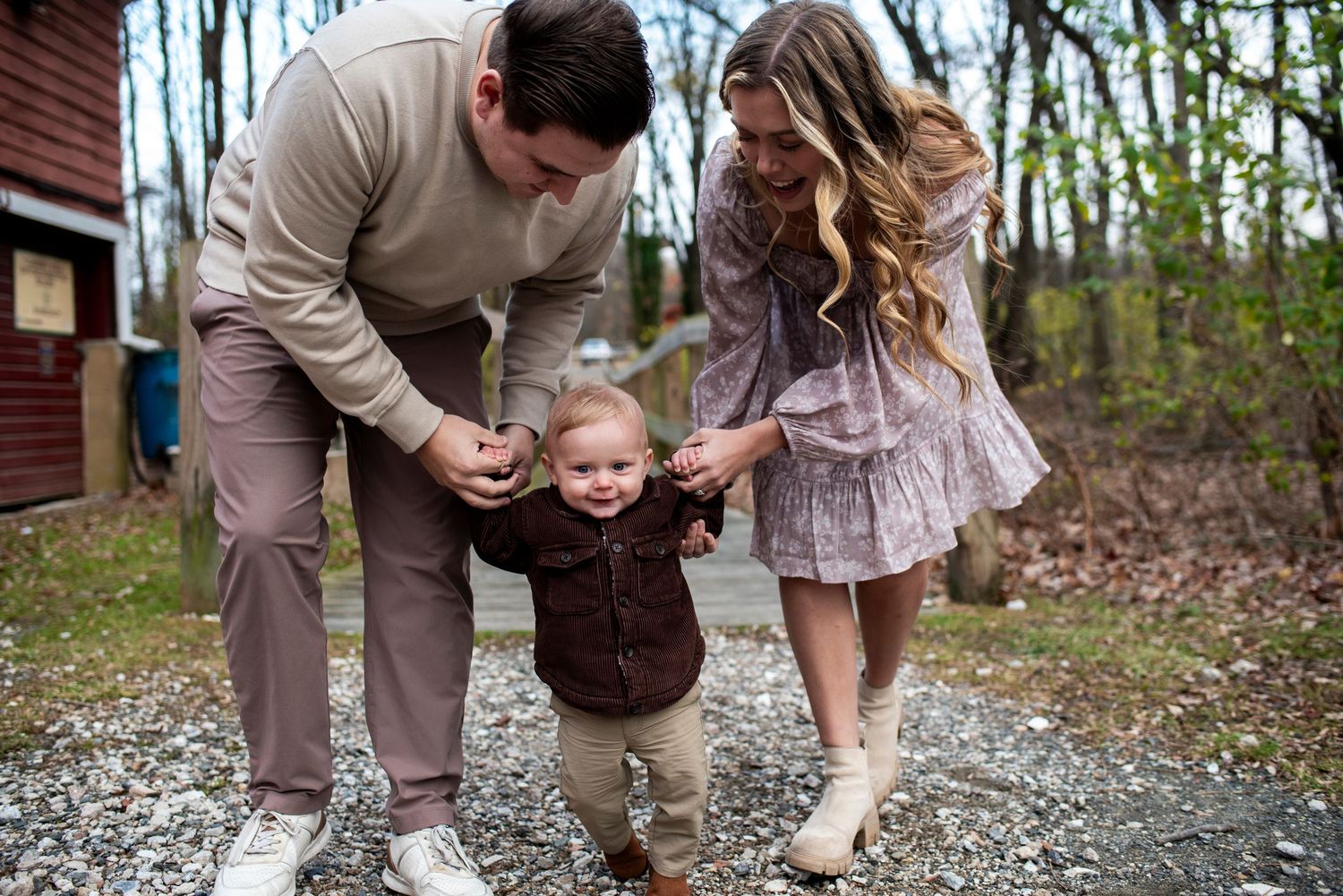 Outdoor portrait of parents helping toddler to walk on a rocky path.