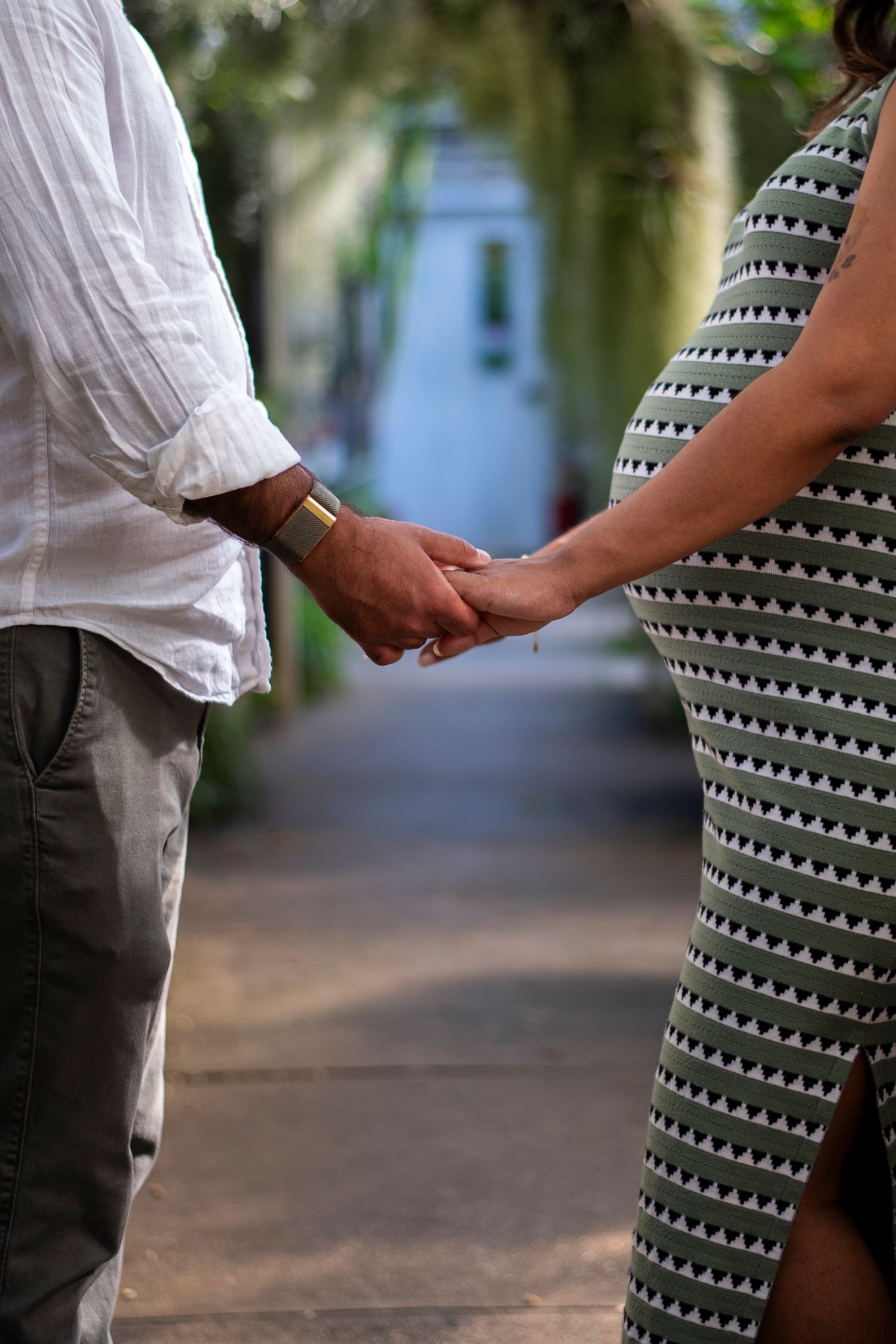 Neck to knee side view of pregnant couple holding hands in greenhouse at Deep Cut Gardens in New Jersey.