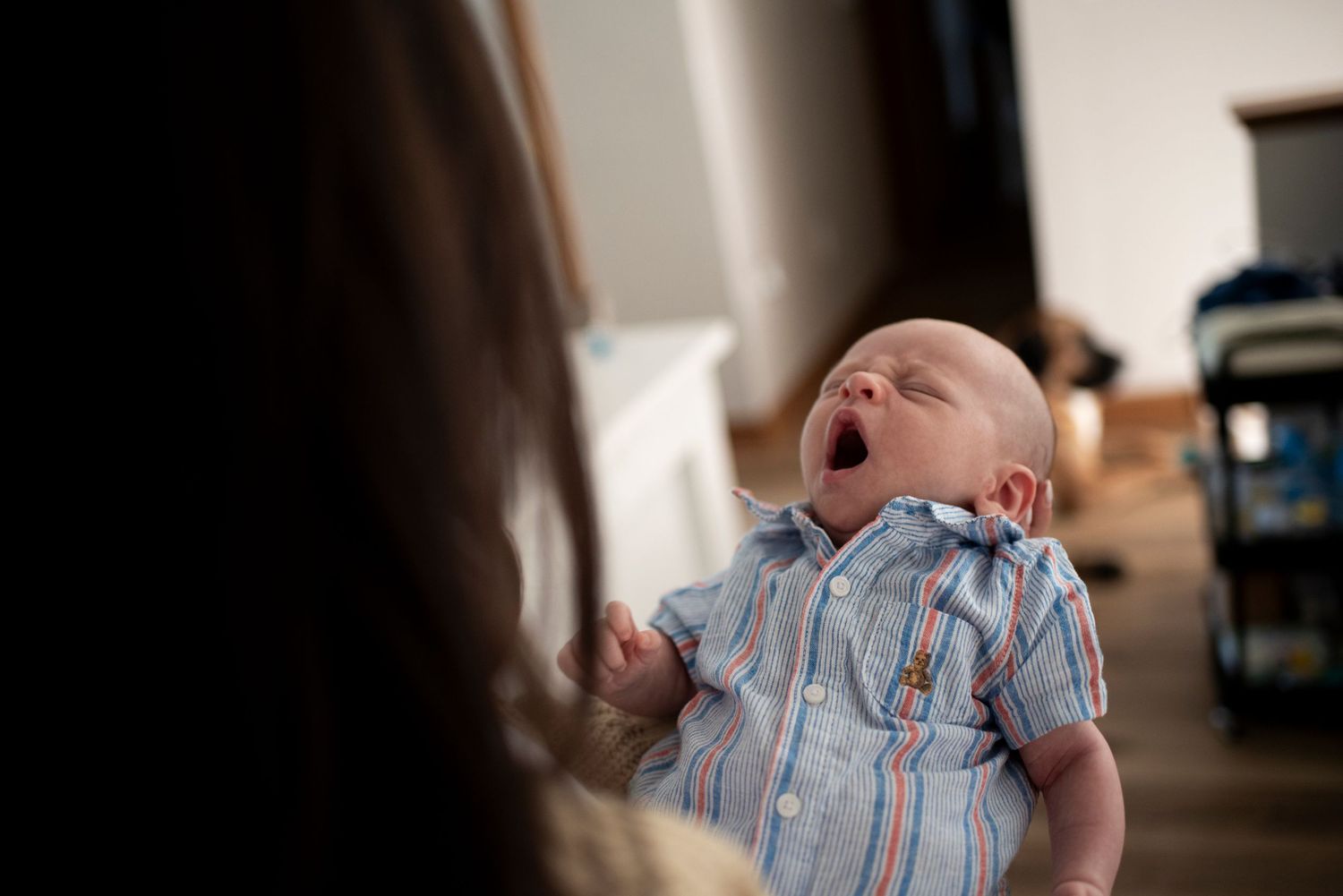 Newborn baby yawns in his mother's arms.