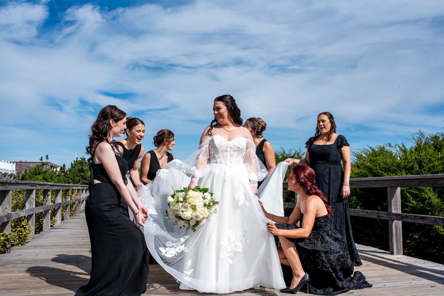 Bridal party in black dresses fluff the bride's dress on the boardwalk in Stone Harbor, New Jersey.