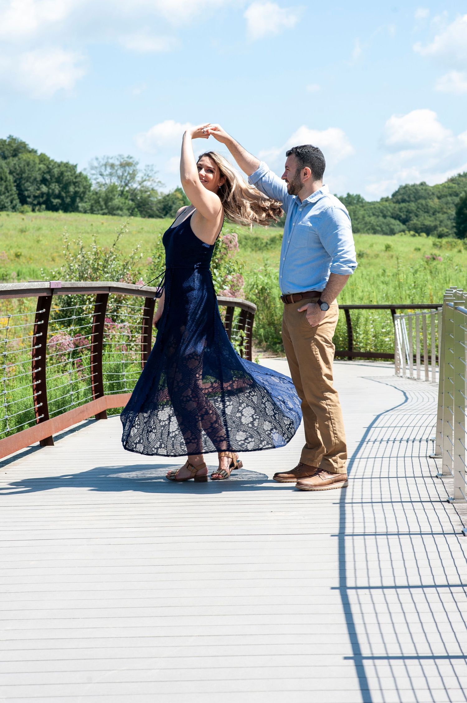 Engaged couple twirls on a bridge through a beautiful field at Longwood Gardens in Pennsylvania.