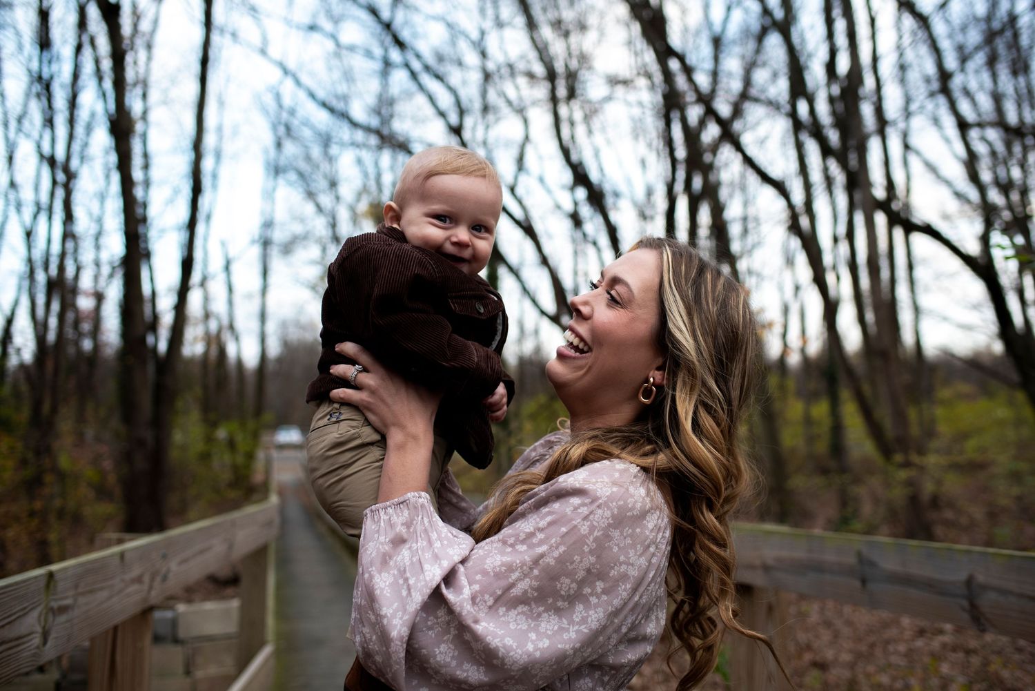 Outdoor portrait of mom lifting her smiling toddler up in the air.