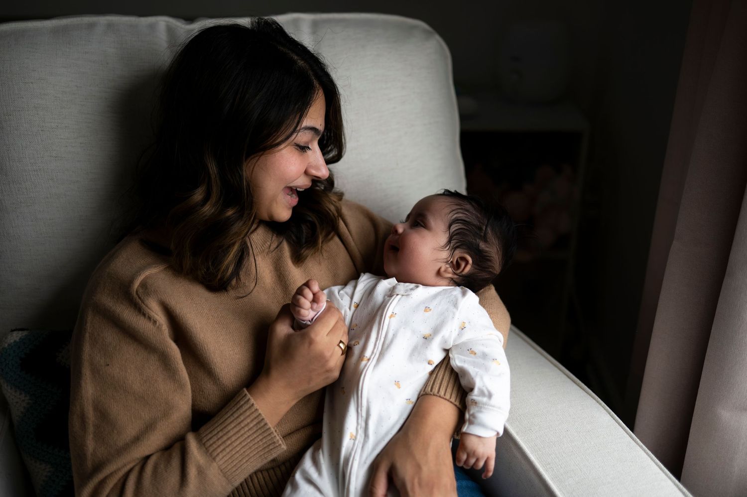New mother and baby girl smile at each other in their nursery chair in New Jersey.