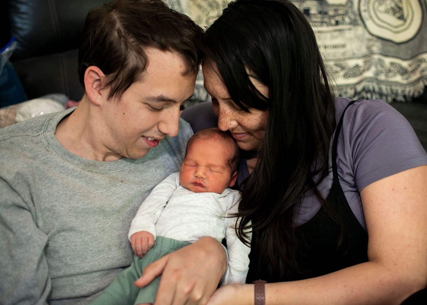 New parents smile down at their newborn son resting in their arms.