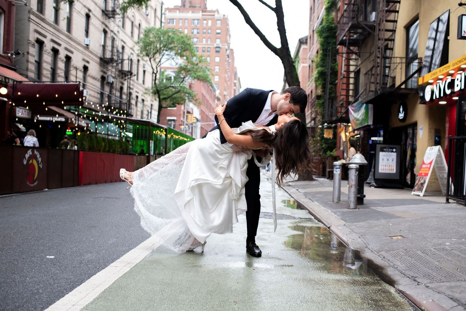 Groom dips bride for a kiss in a rainy New York City street outside of Cafe Wha? before their wedding reception.