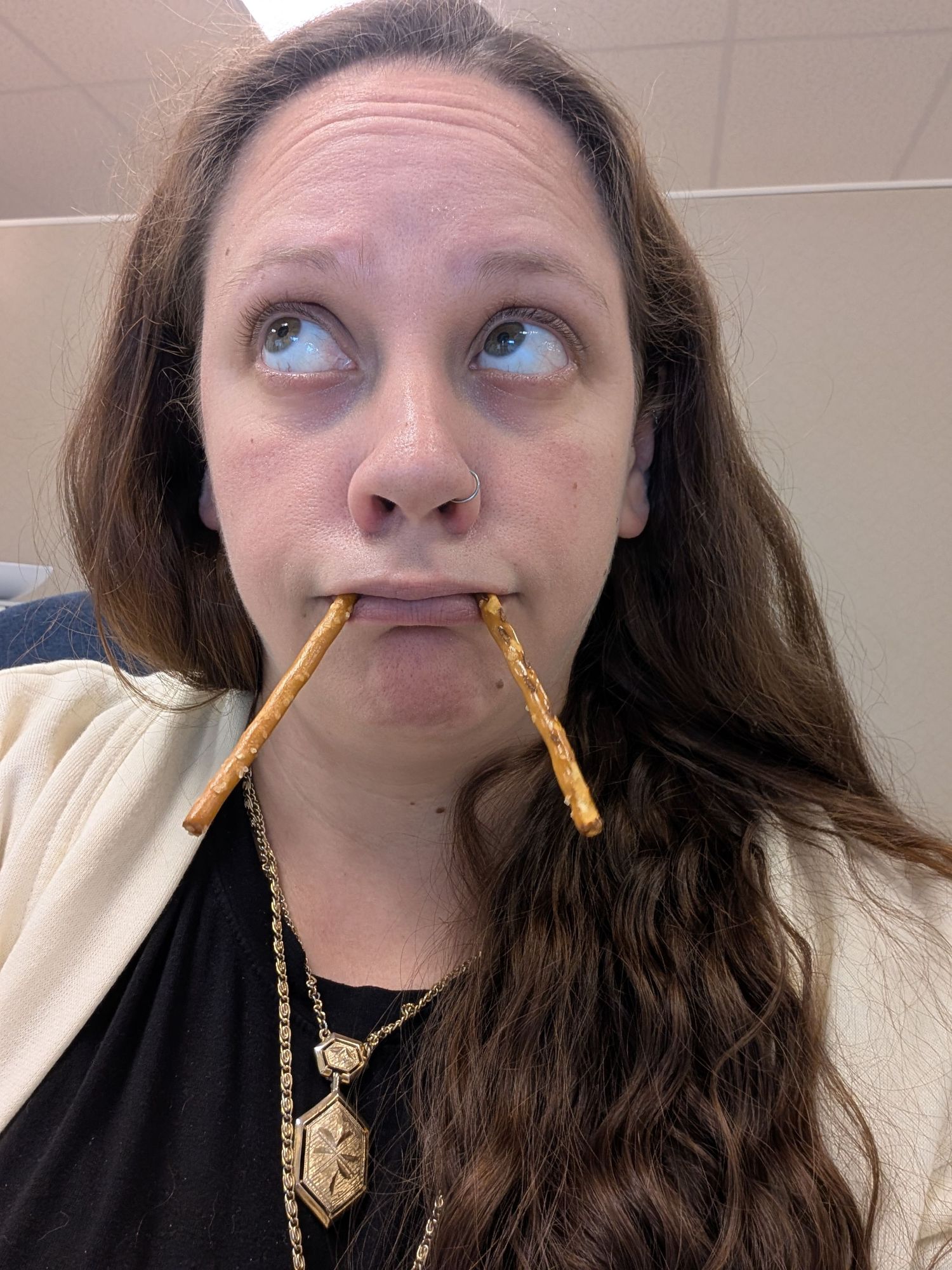 Selfie of woman with long, wavy hair using pretzel sticks as pretend walrus tusks.
