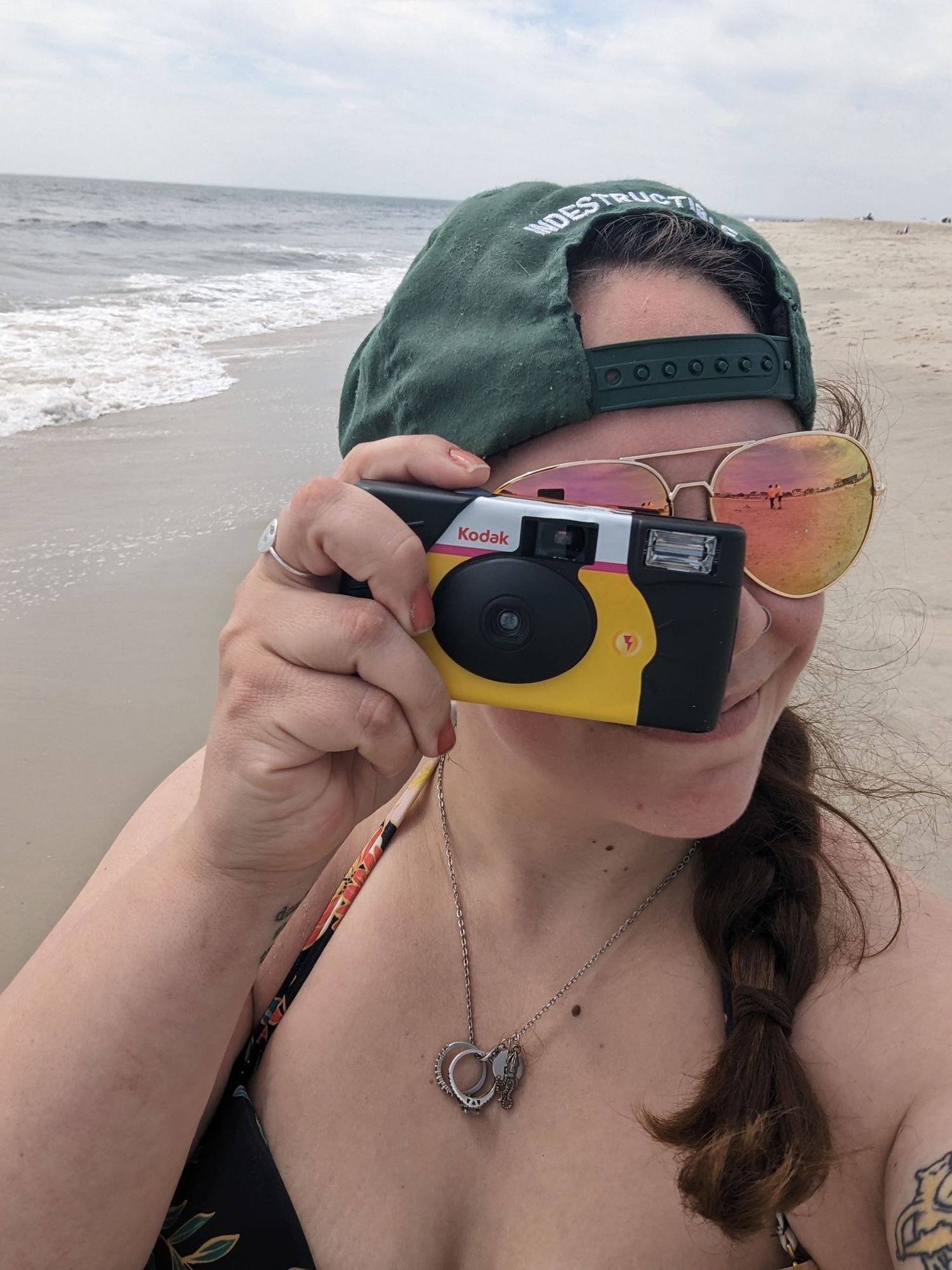 Selfie of woman on the beach taking a photo with a disposable camera.