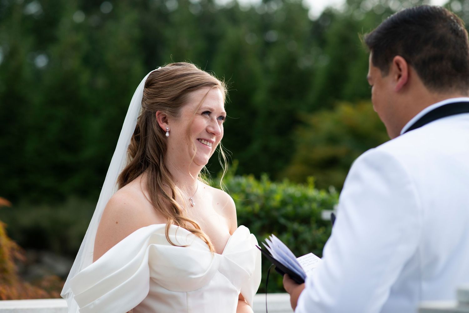 Bride smiles as groom reads his vows in the garden at the Mansion in Voorhees, New Jersey.
