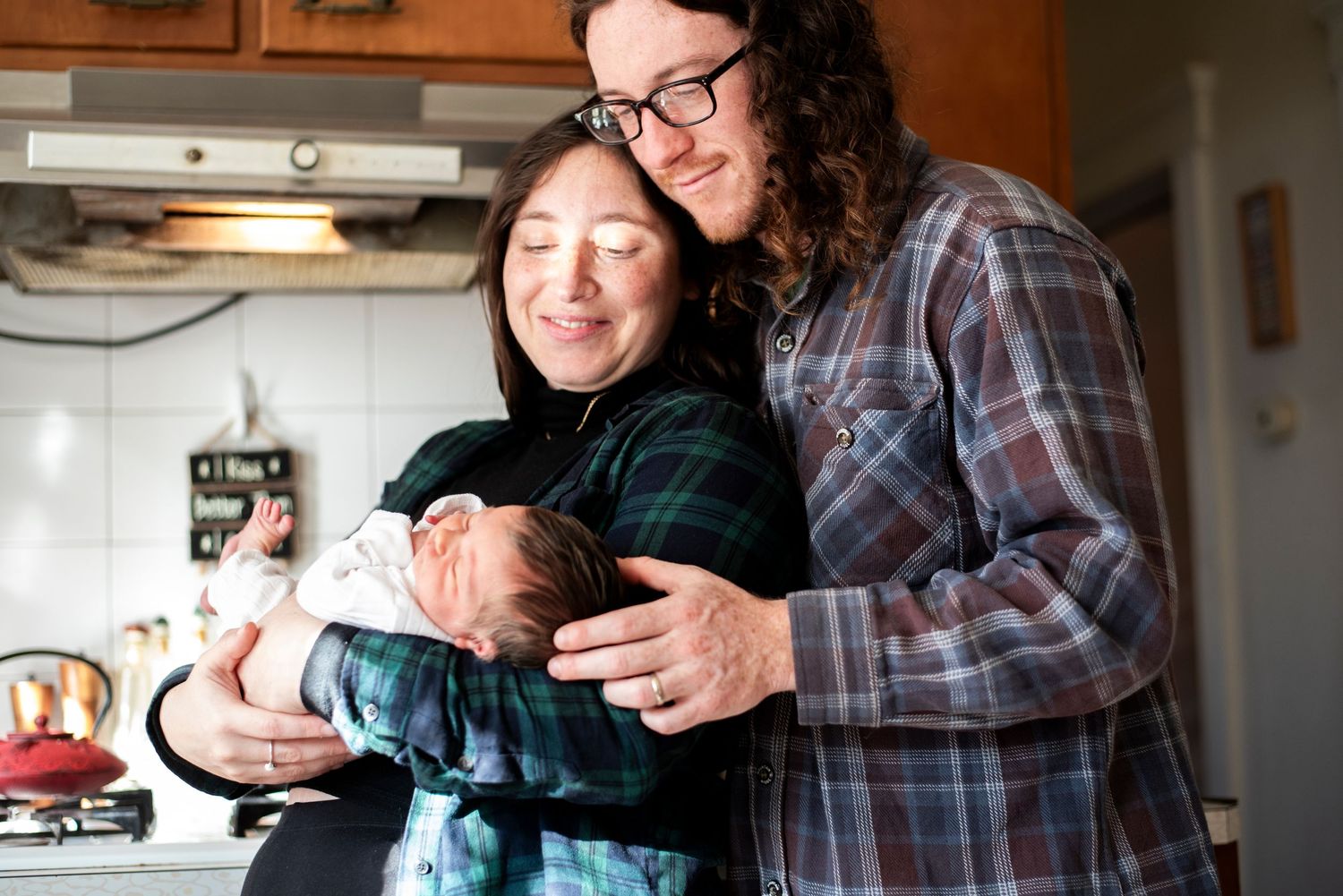 New mom and dad smile down at their newborn baby girl as they hold her in their kitchen in Highland Park, New Jersey.