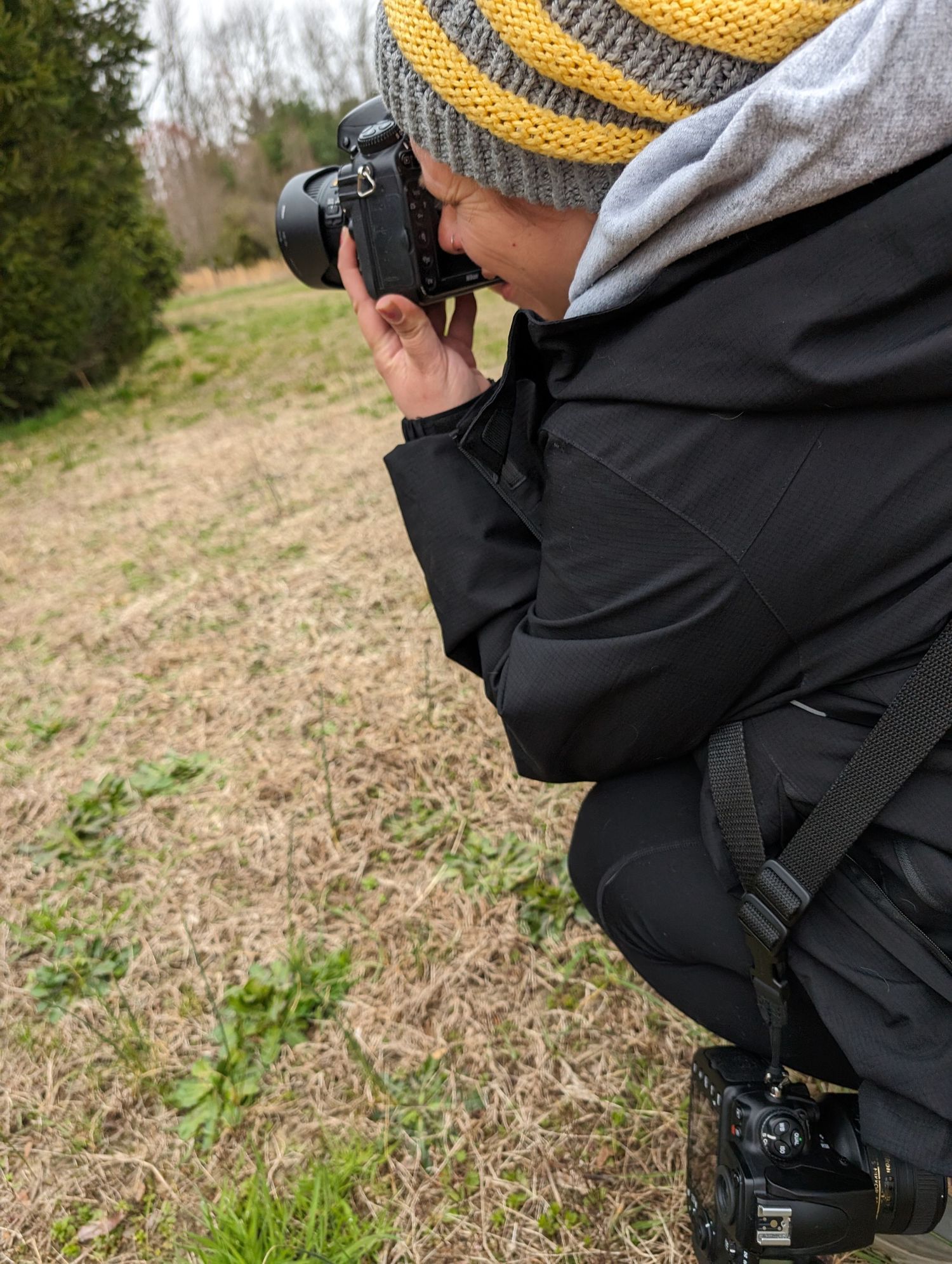 Side photo of woman in yellow and gray striped winter hat squatting to take a photo.