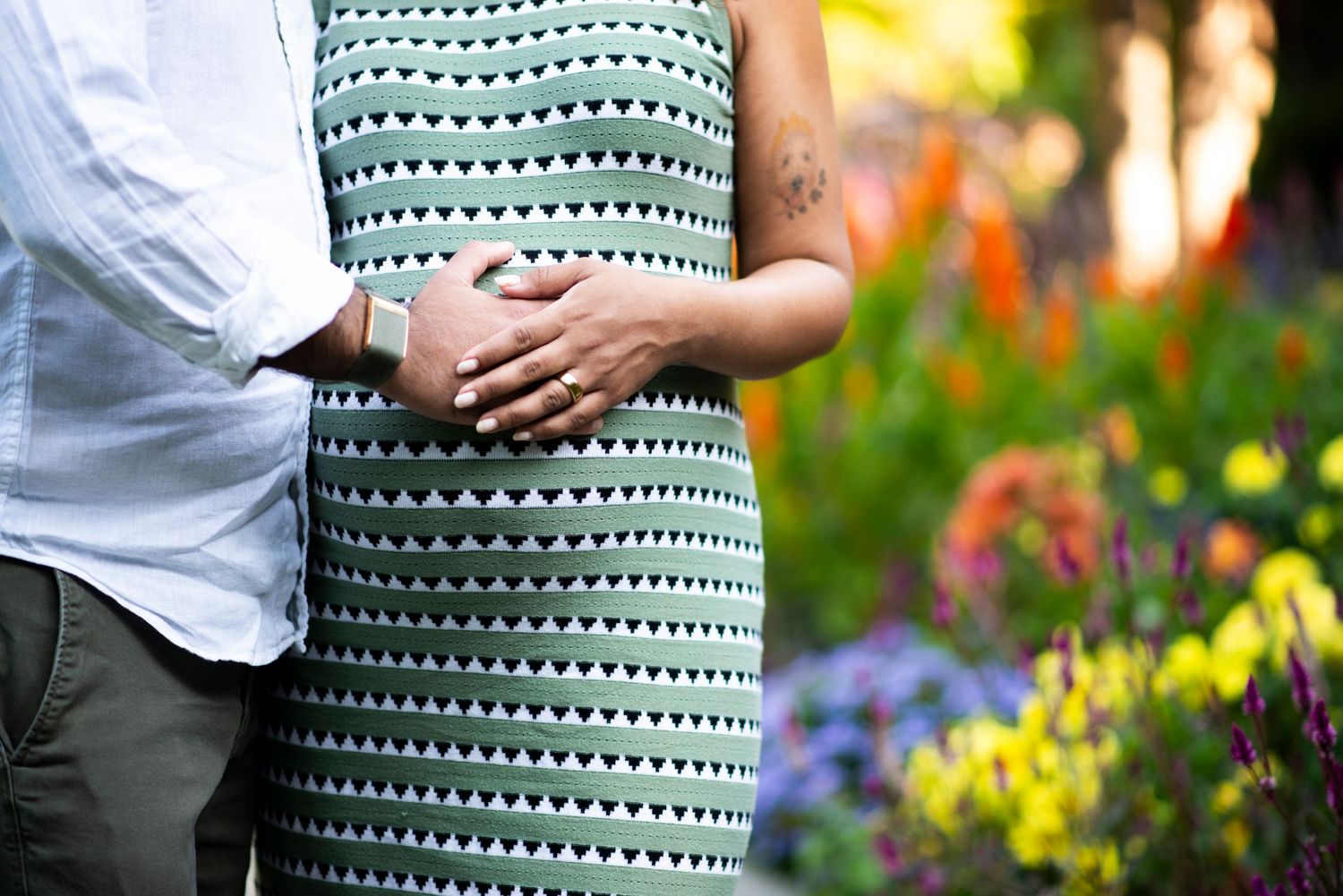 Close up of hands on pregnant belly in front of colorful flowers at Deep Cut Gardens in New Jersey.
