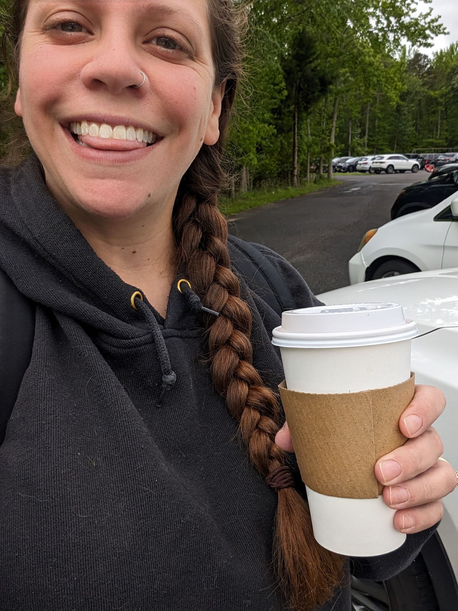 Selfie of woman smiling in parking lot holding non-branded coffee to-go cup.