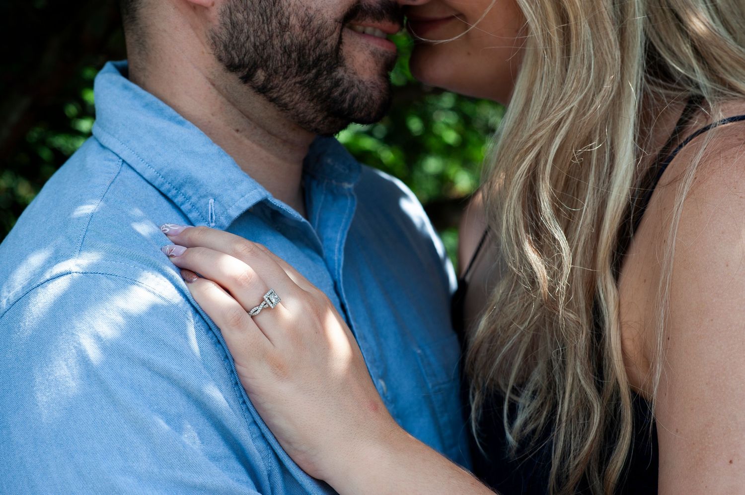 Close up of woman's hand on future husband's chest, showing off her engagement ring.