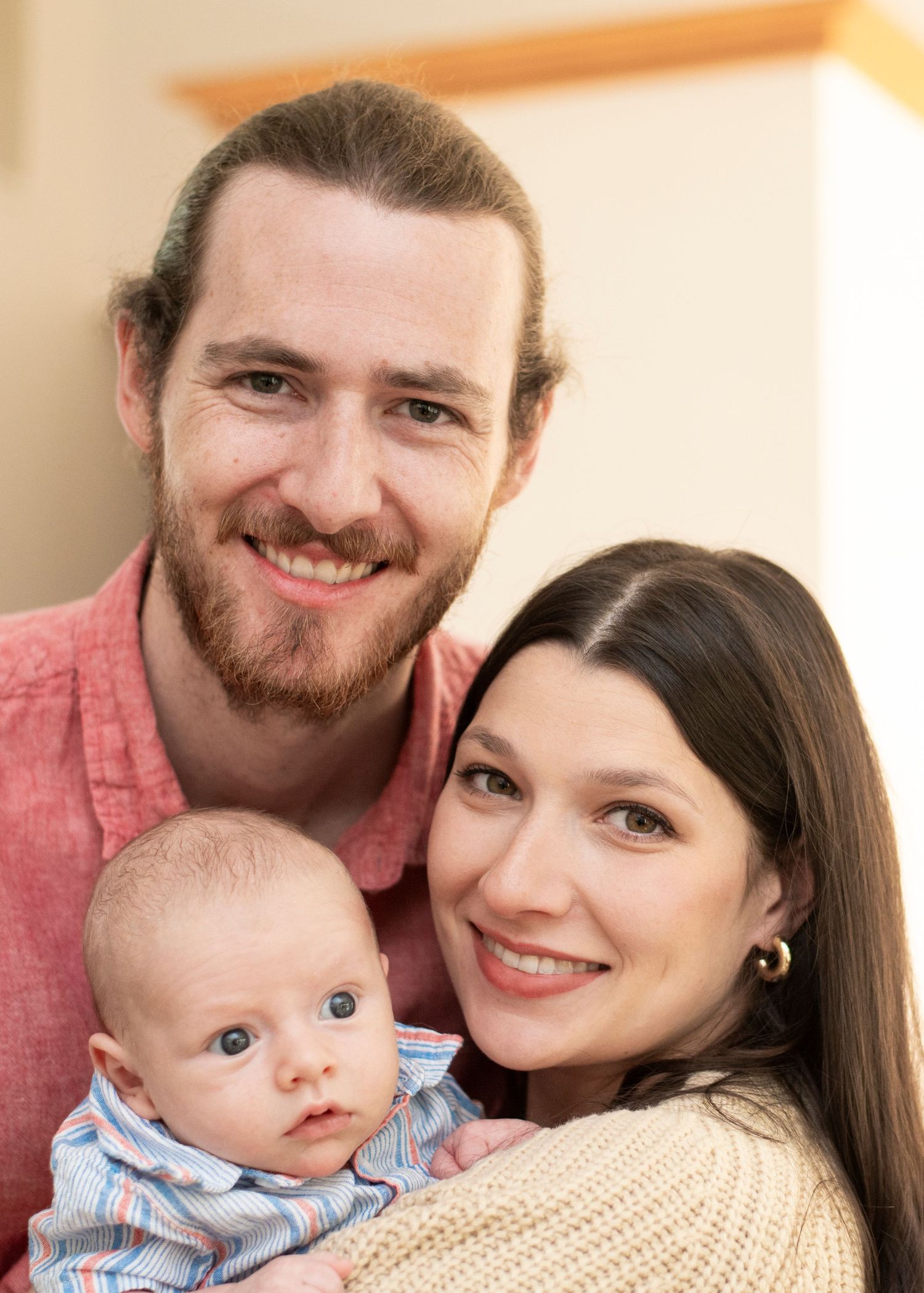 Portrait of new parents and newborn baby smiling at the camera in their home in New Jersey.