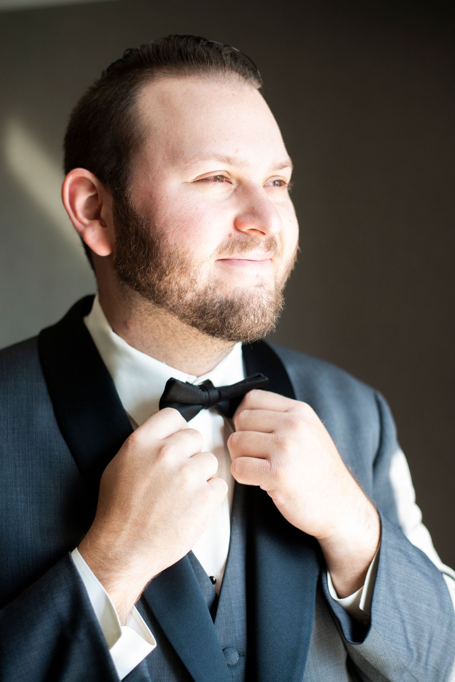 Groom adjusts his bowtie in the window light before his wedding at Hamilton Manor in New Jersey.