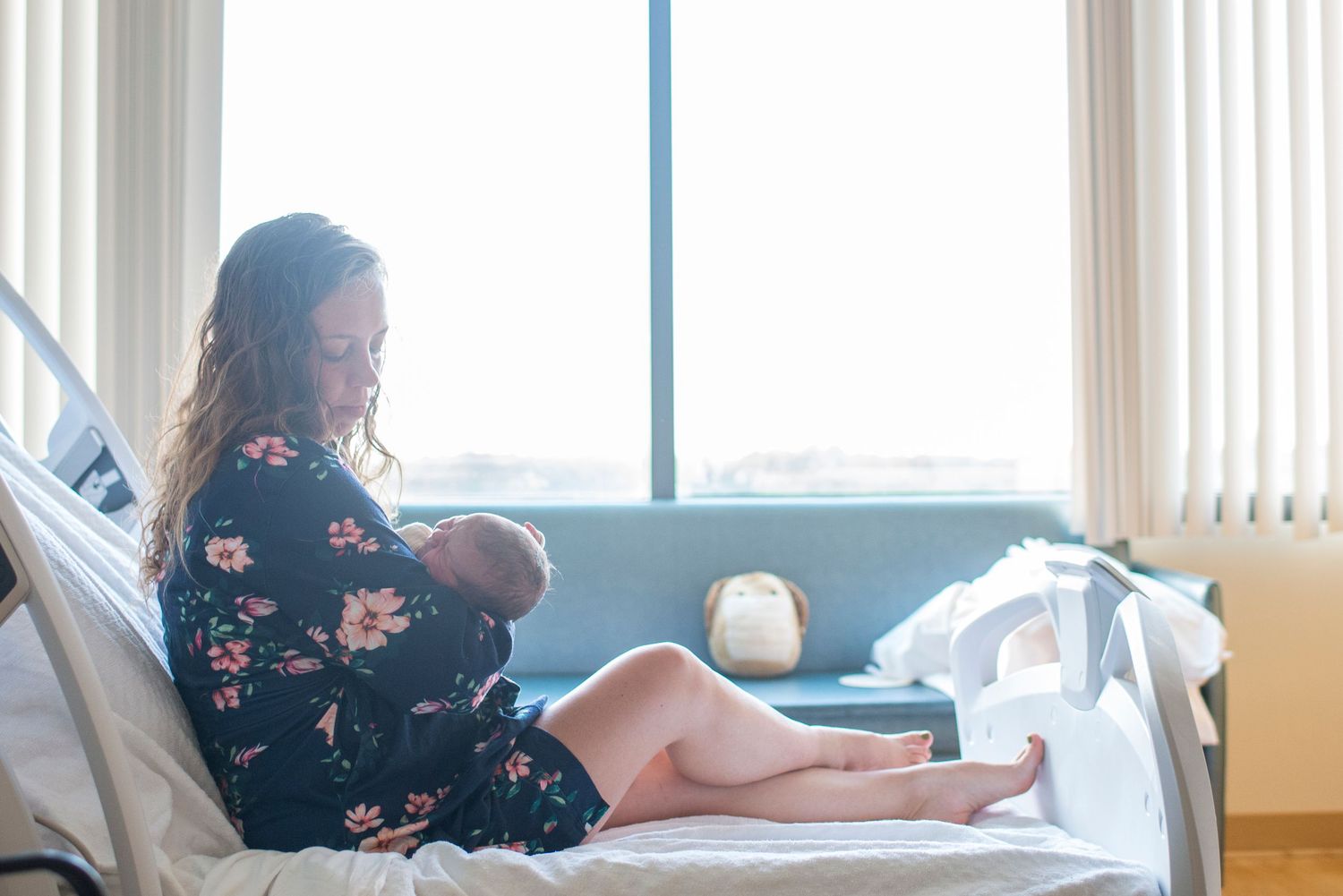 New mom holds her newborn baby in hospital bed silhouetted against the window.