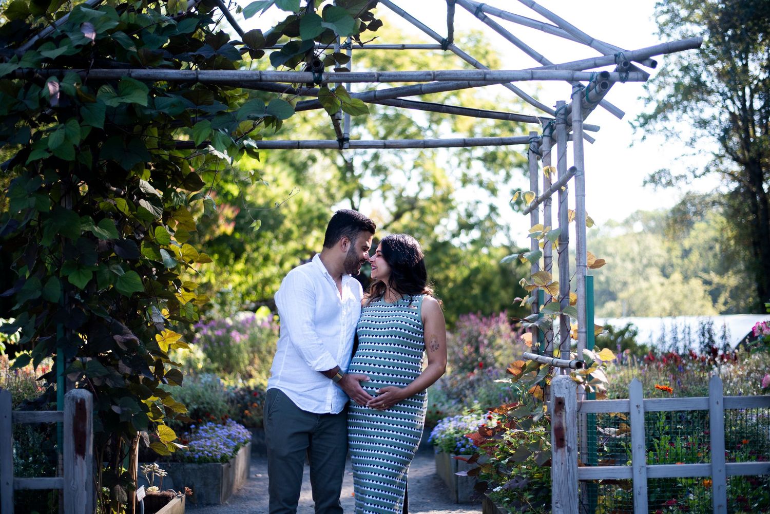 Couple smile nose to nose at the garden entrance at Deep Cut Gardens in New Jersey during maternity shoot.
