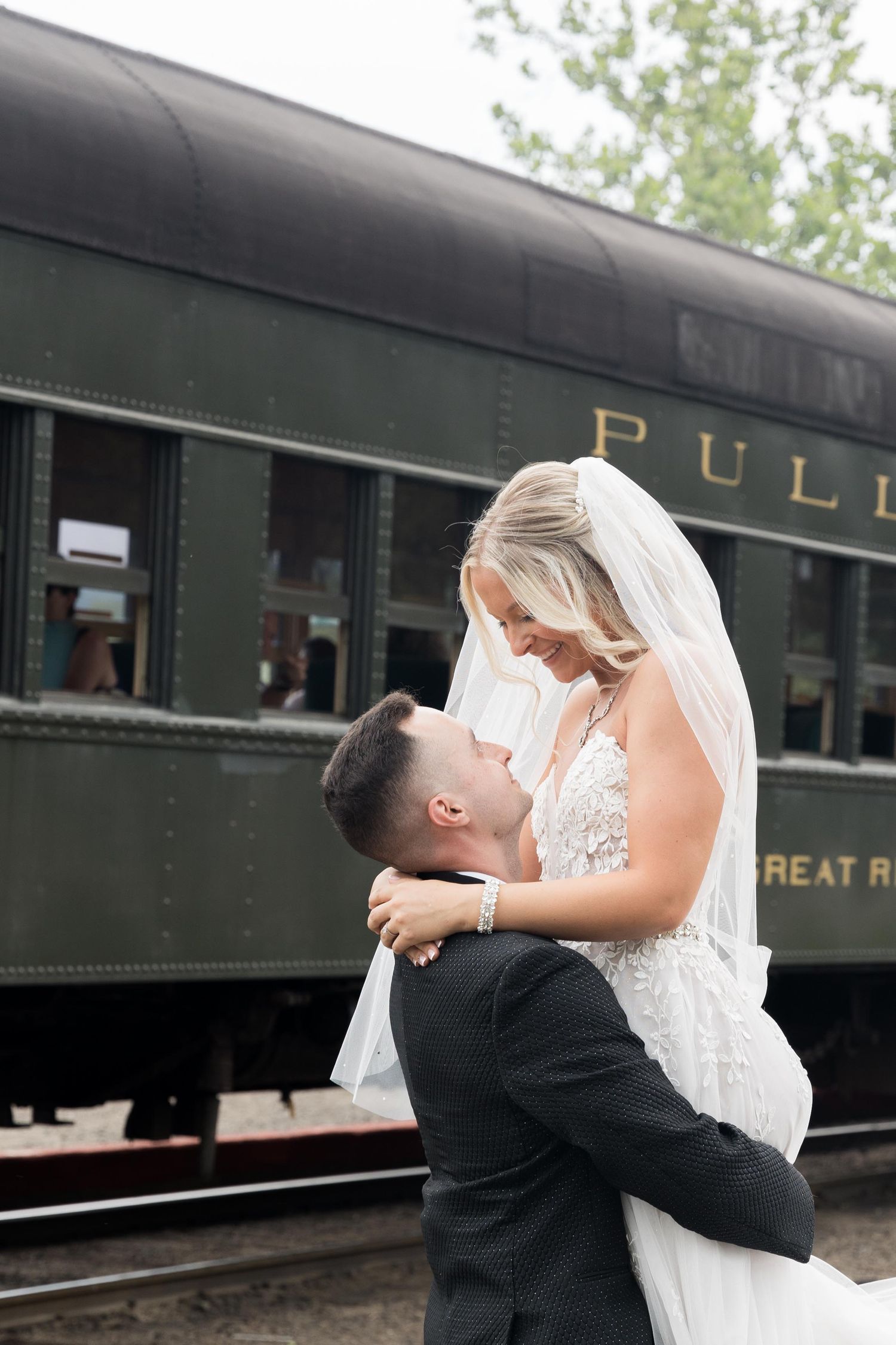 A romantic wedding moment captured in front of a vintage Pullman train car on a historic railway.