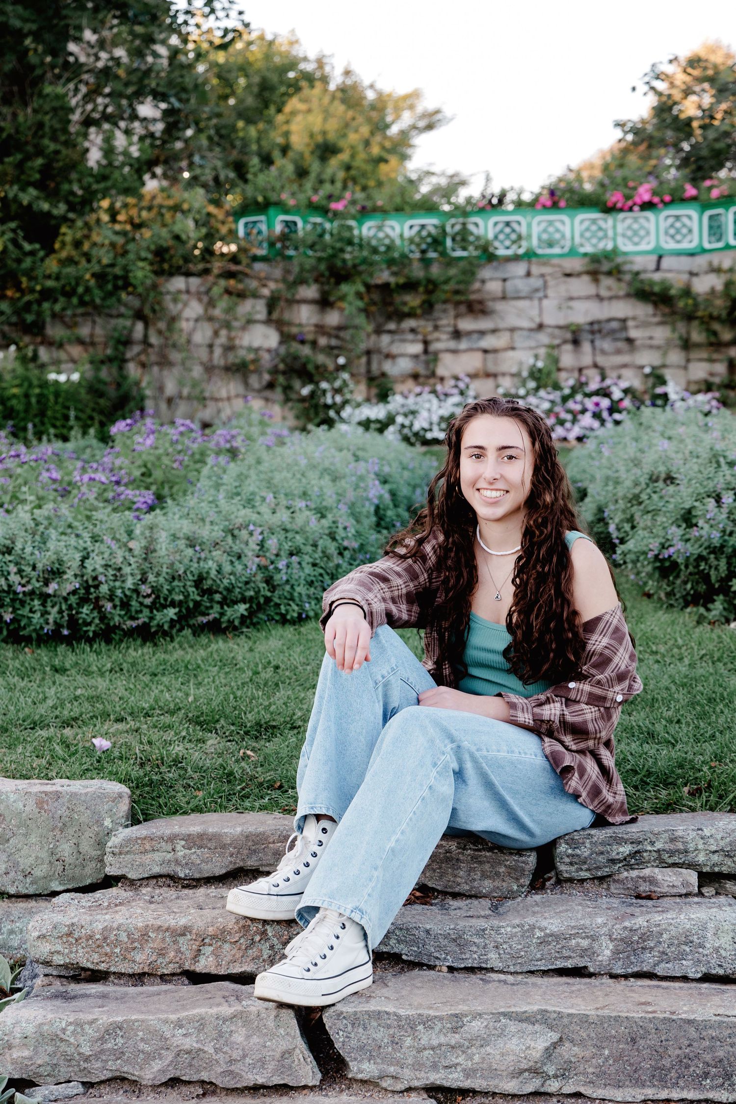 A casual outdoor portrait session on stone steps with flowers and greenery in the background.